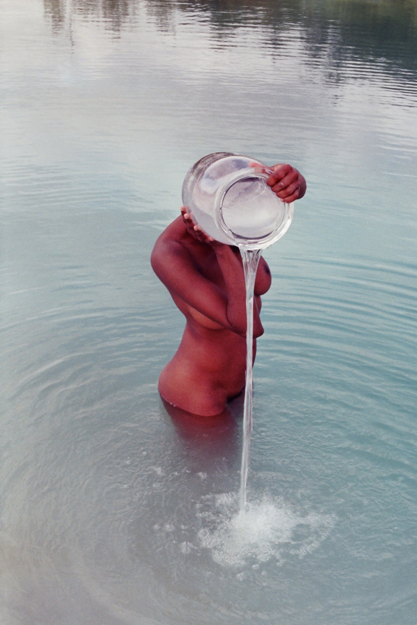 A nude woman pouring water from a jar into a lake.