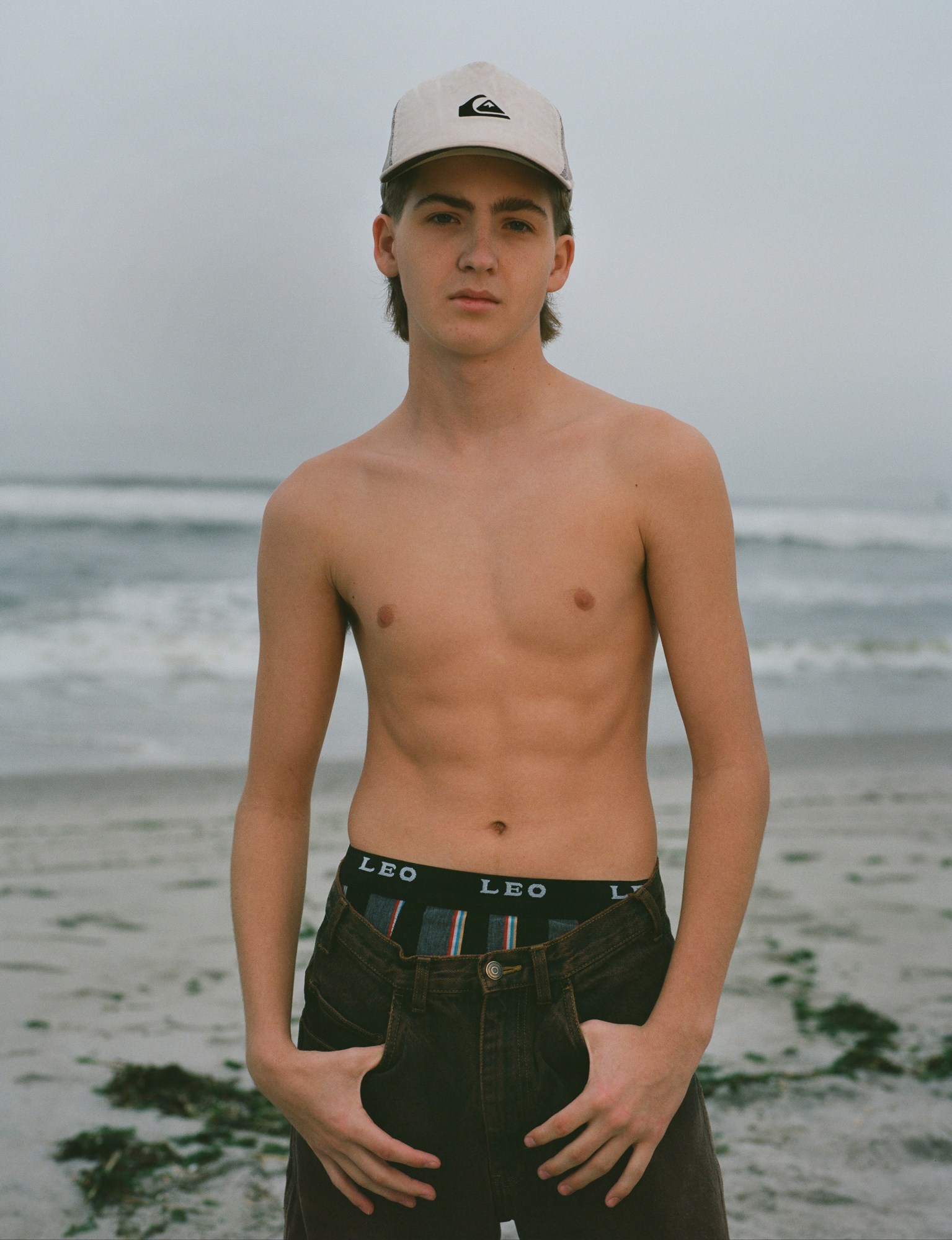 A topless cap-wearing man on a sandy beach