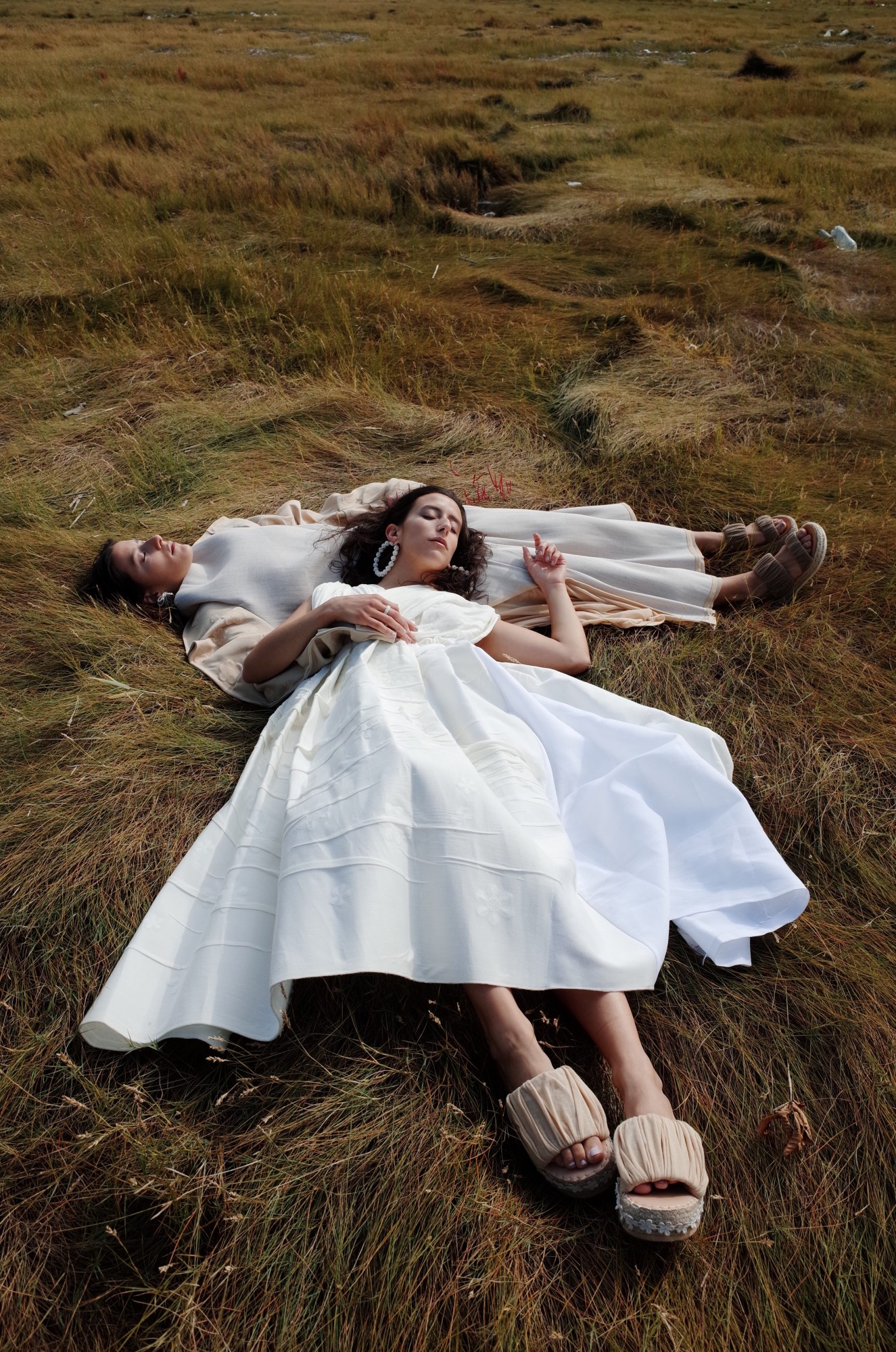 two models laying in the grass in dresses by bingjin zhu