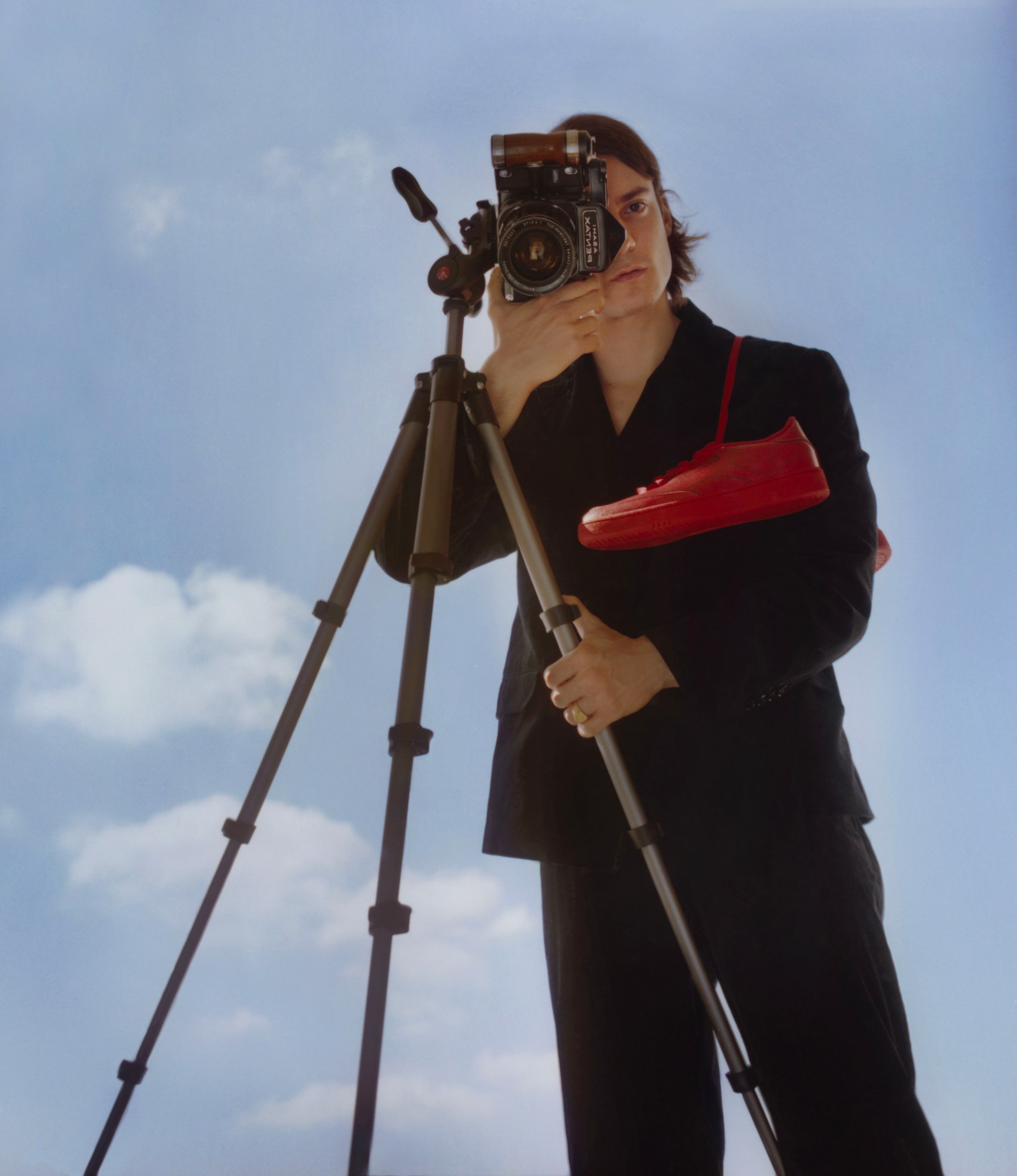 A man shoots a self-portrait against a blue sky with shoes over his shoulder