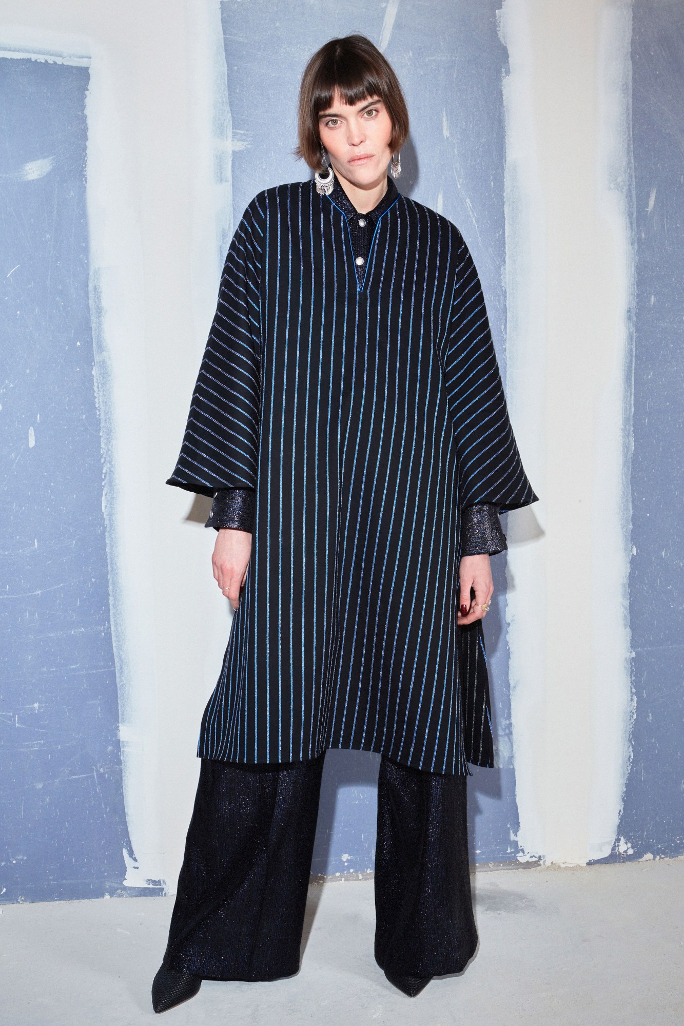 model wearing a black tunic woven with shiny blue vertical stripes, over a pair of dark trousers. clothes by Benjamin Benmoyal