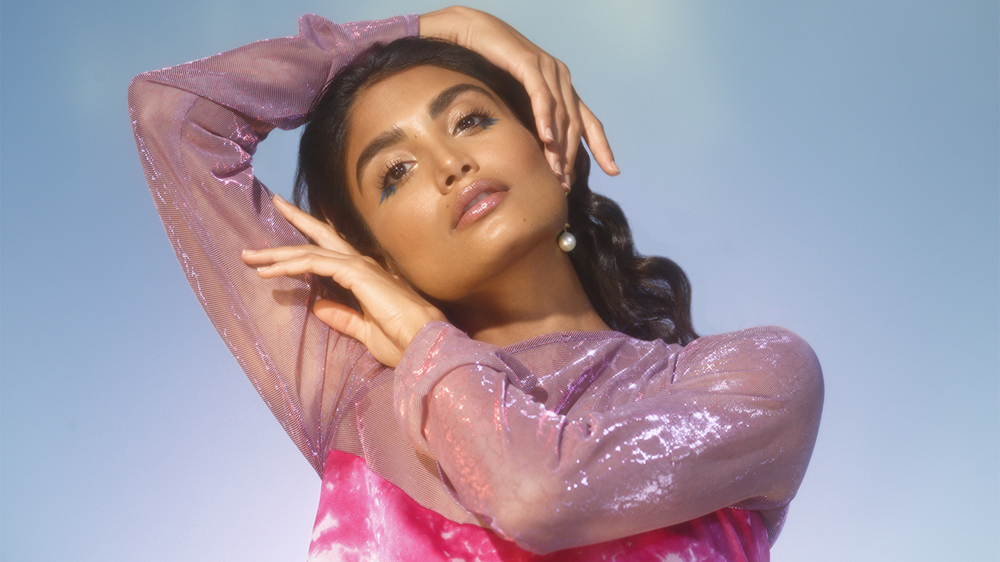 Woman in pink shimmery top framing her face with her hands