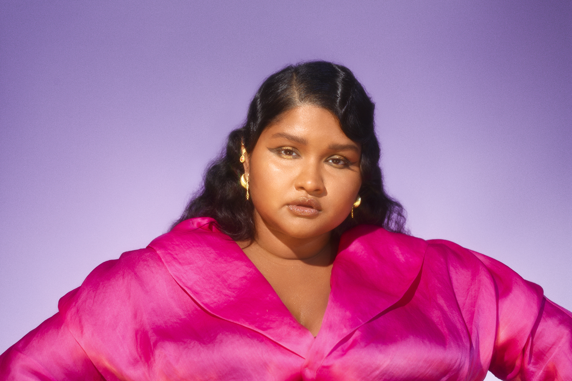 Woman stares at the camera in pink shirt with gold earrings