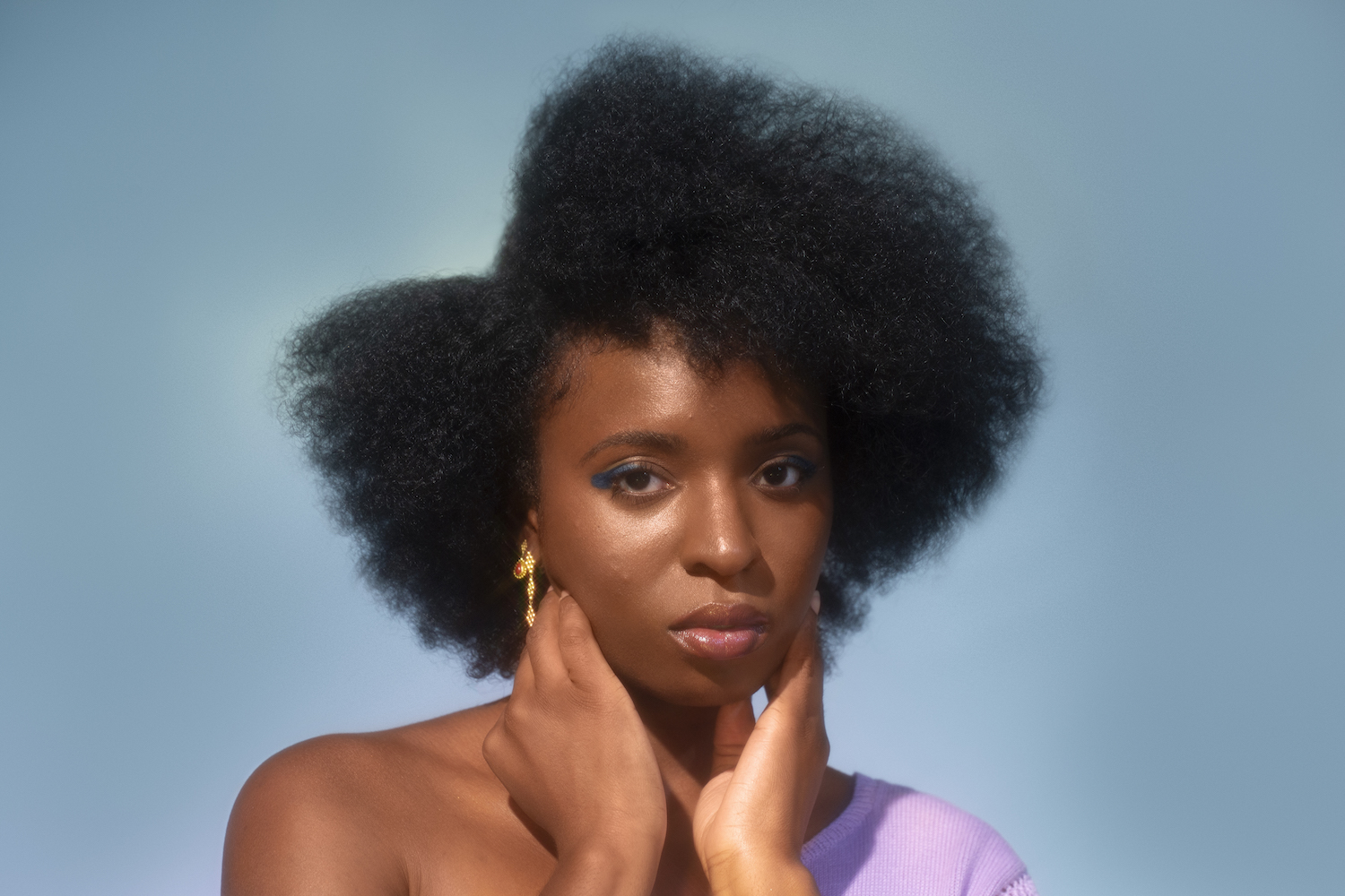 Woman framing face with hands in purple one shoulder top