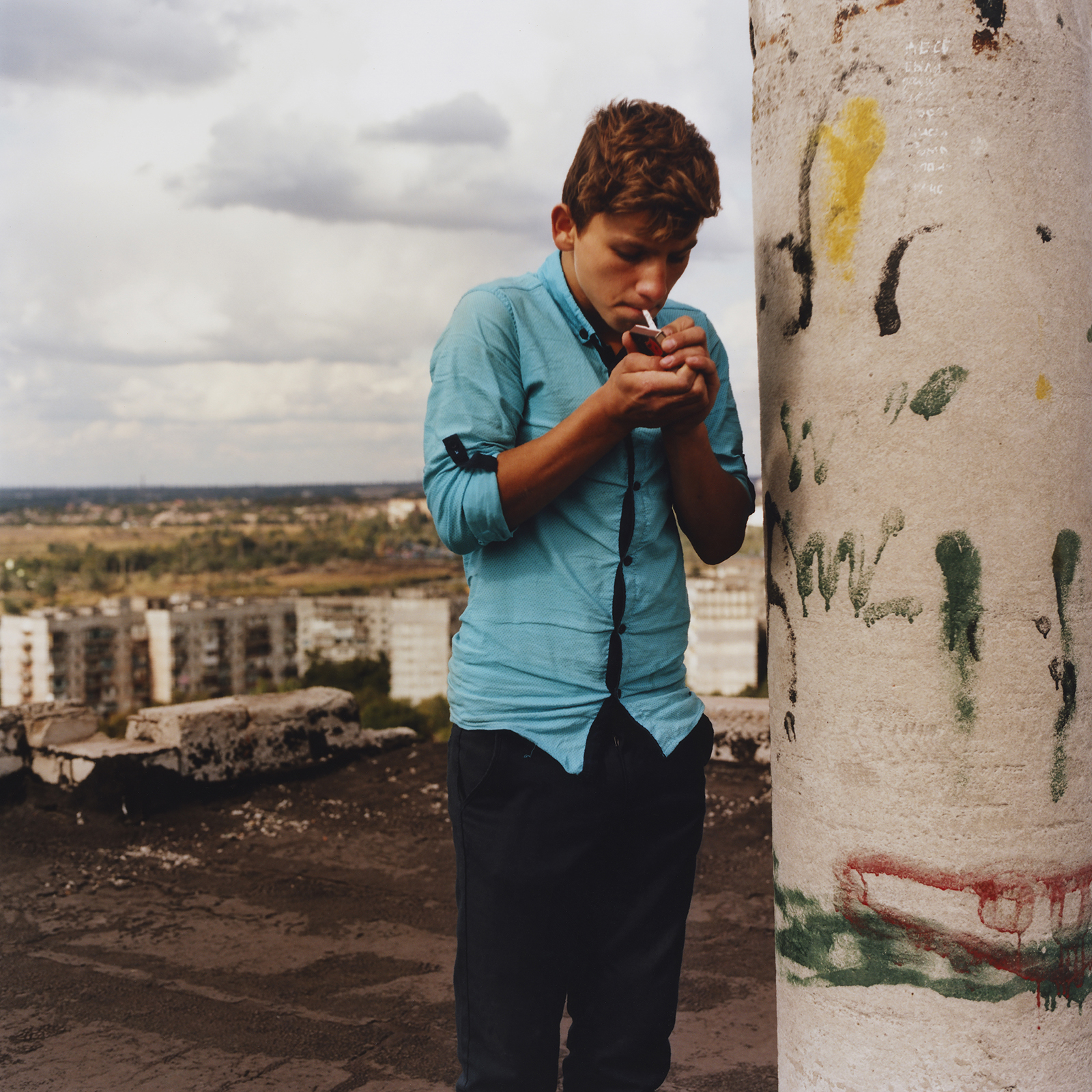 a young man lights a cigarette on the roof of a building