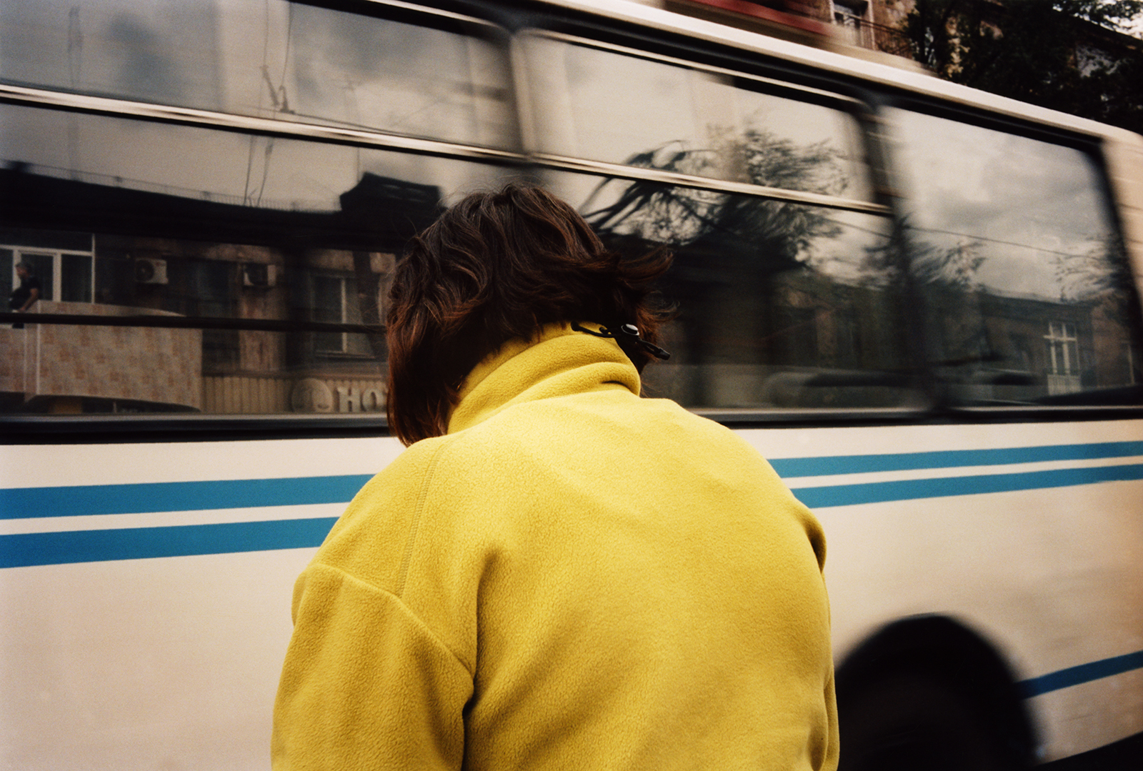 a woman in a yellow fleece faces a bus that drives past