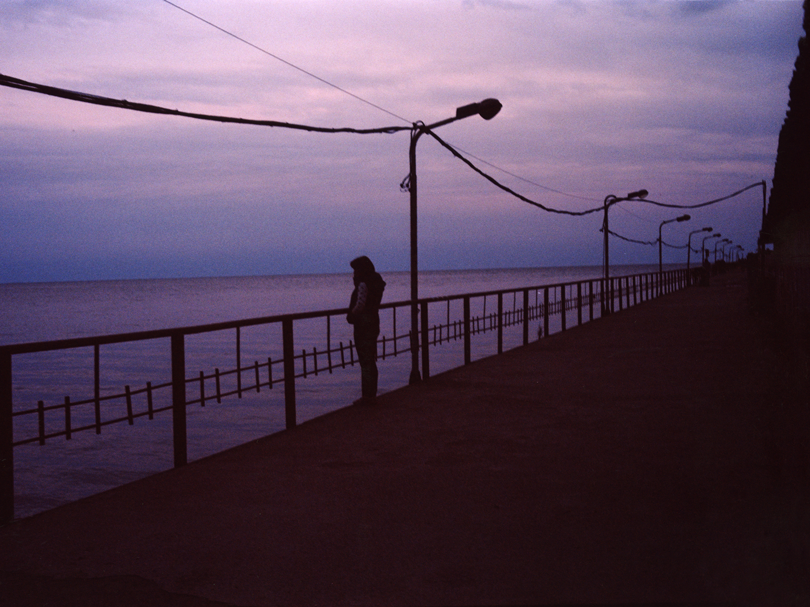 the silhouette of a person on the sea front as the sun sets