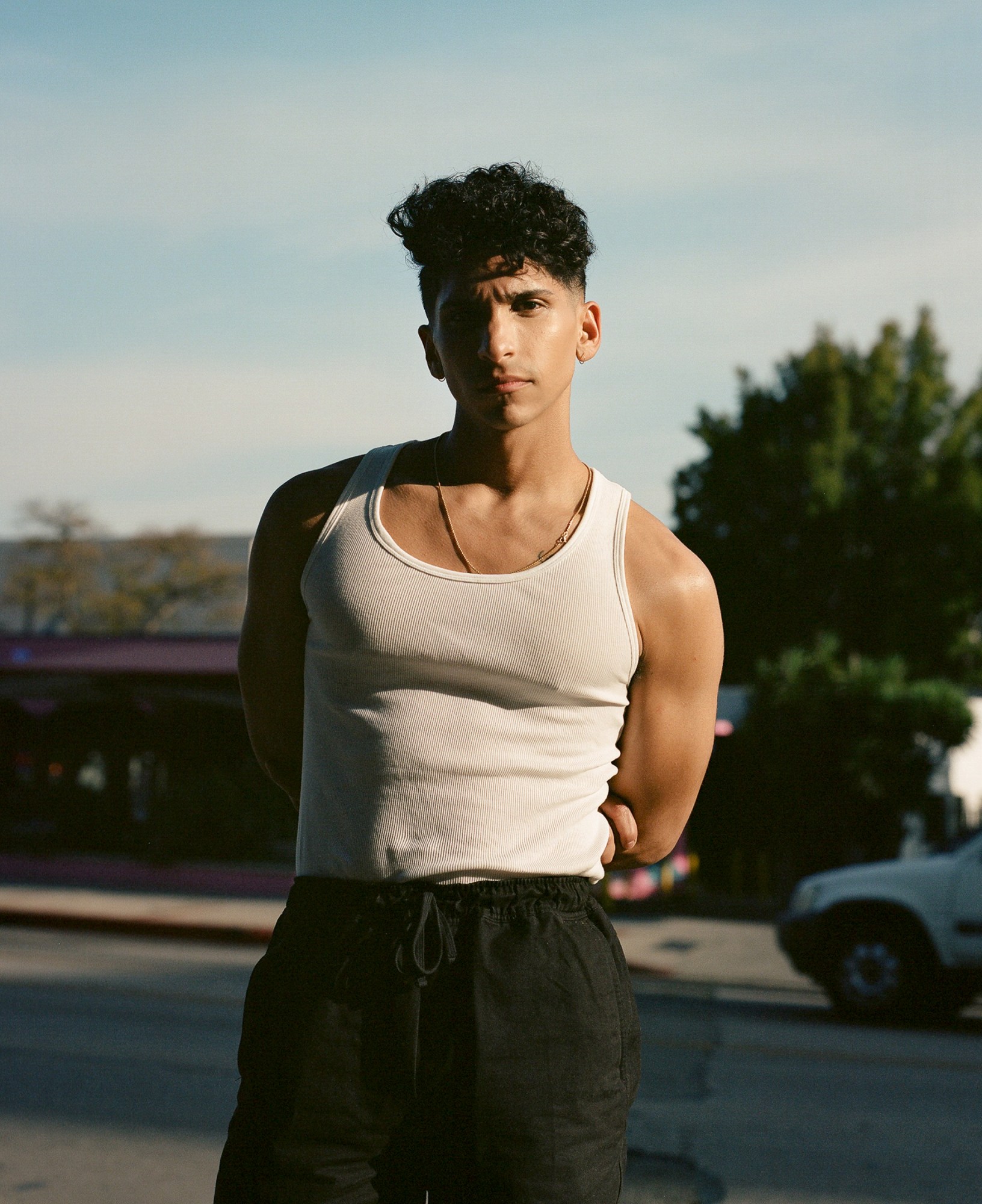 Angel Bismark Curiel, star of Pose, wearing a tank top shot in Los Angeles with trees and cars behind him