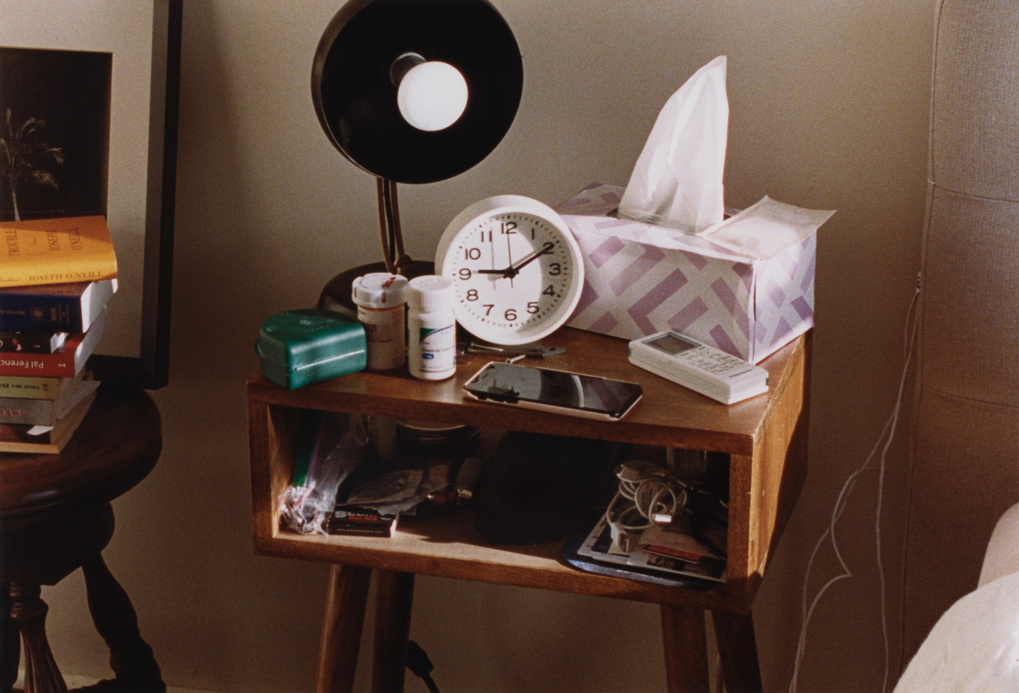 Bedside table with a phone, clock and pills.