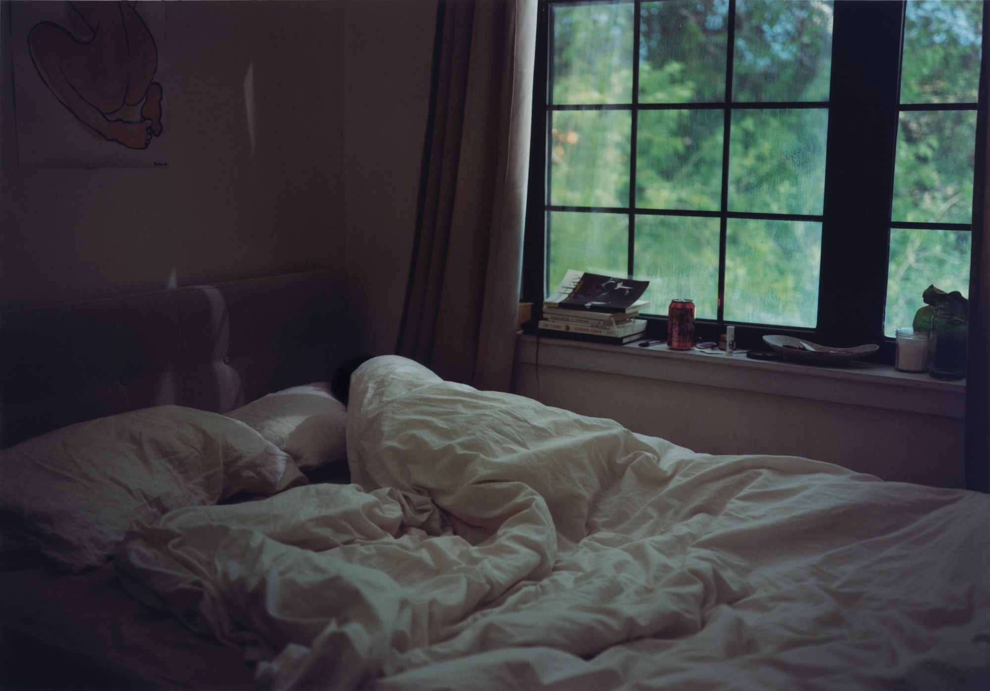 A woman lying wrapped in white blanket in bed in a dark room near a window