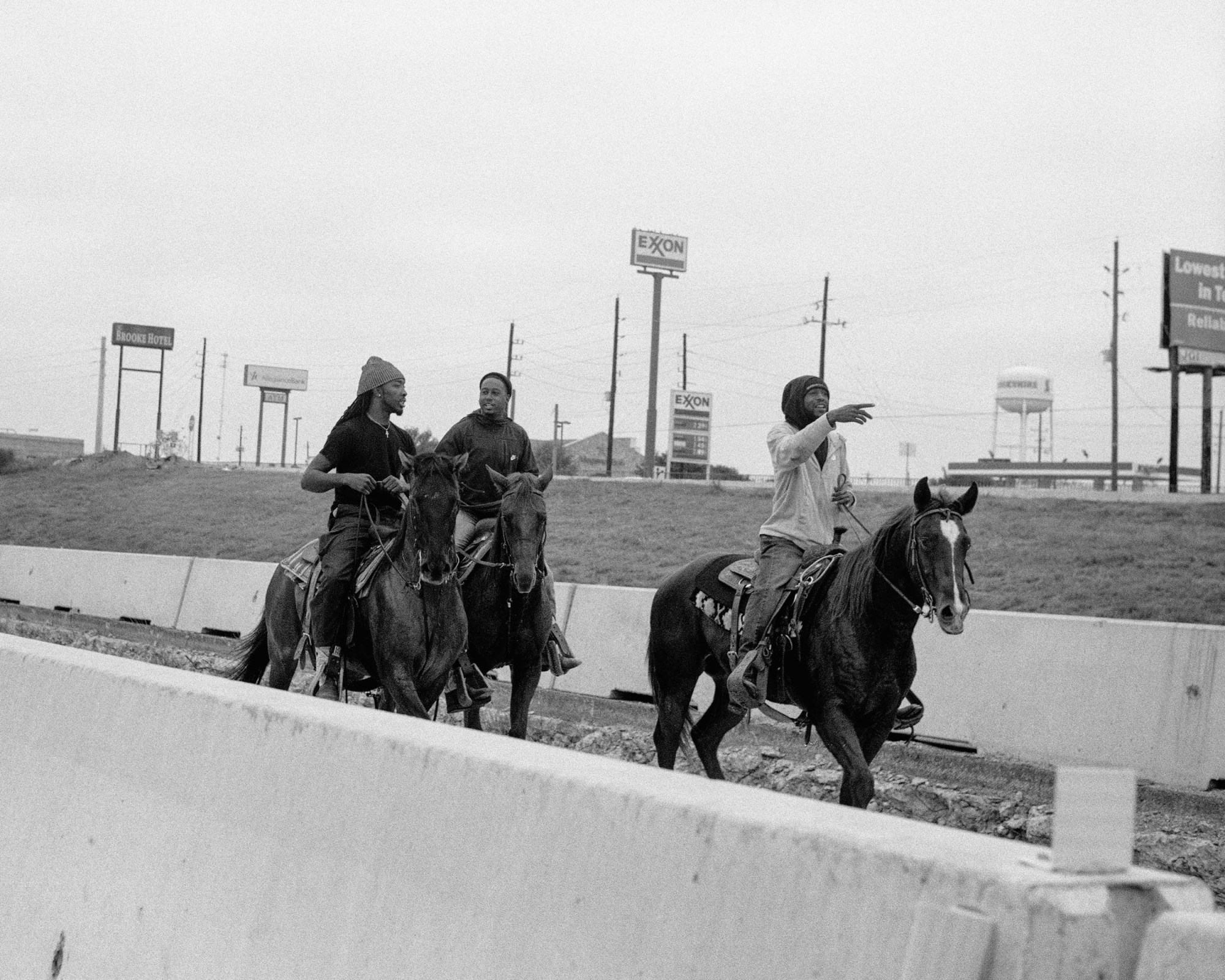 three men on horses walk alongside a highway