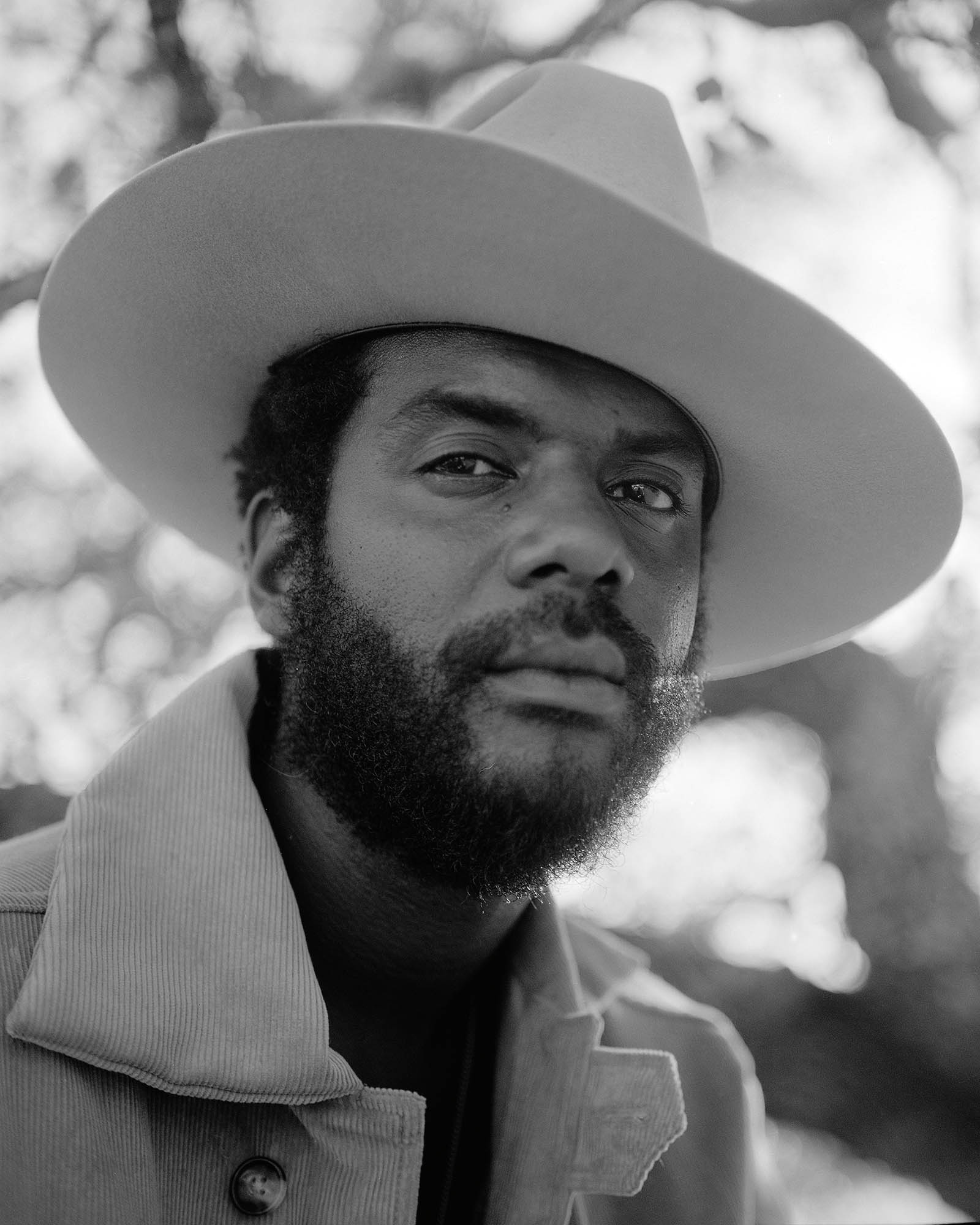 a man in a cowboy hat and a cord jacket looks into the camera