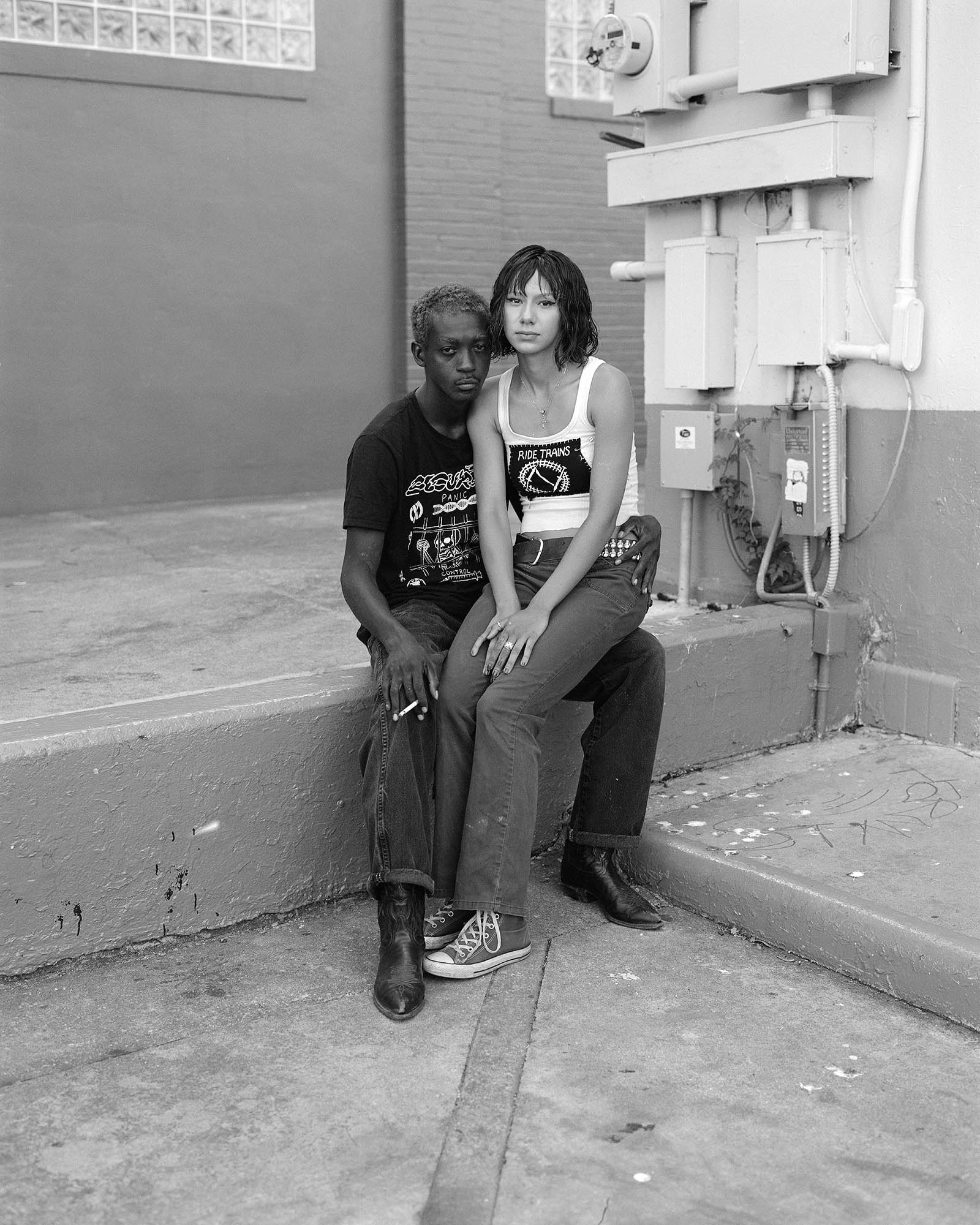 a woman sits on a man's lap on a concrete ridge behind a bu