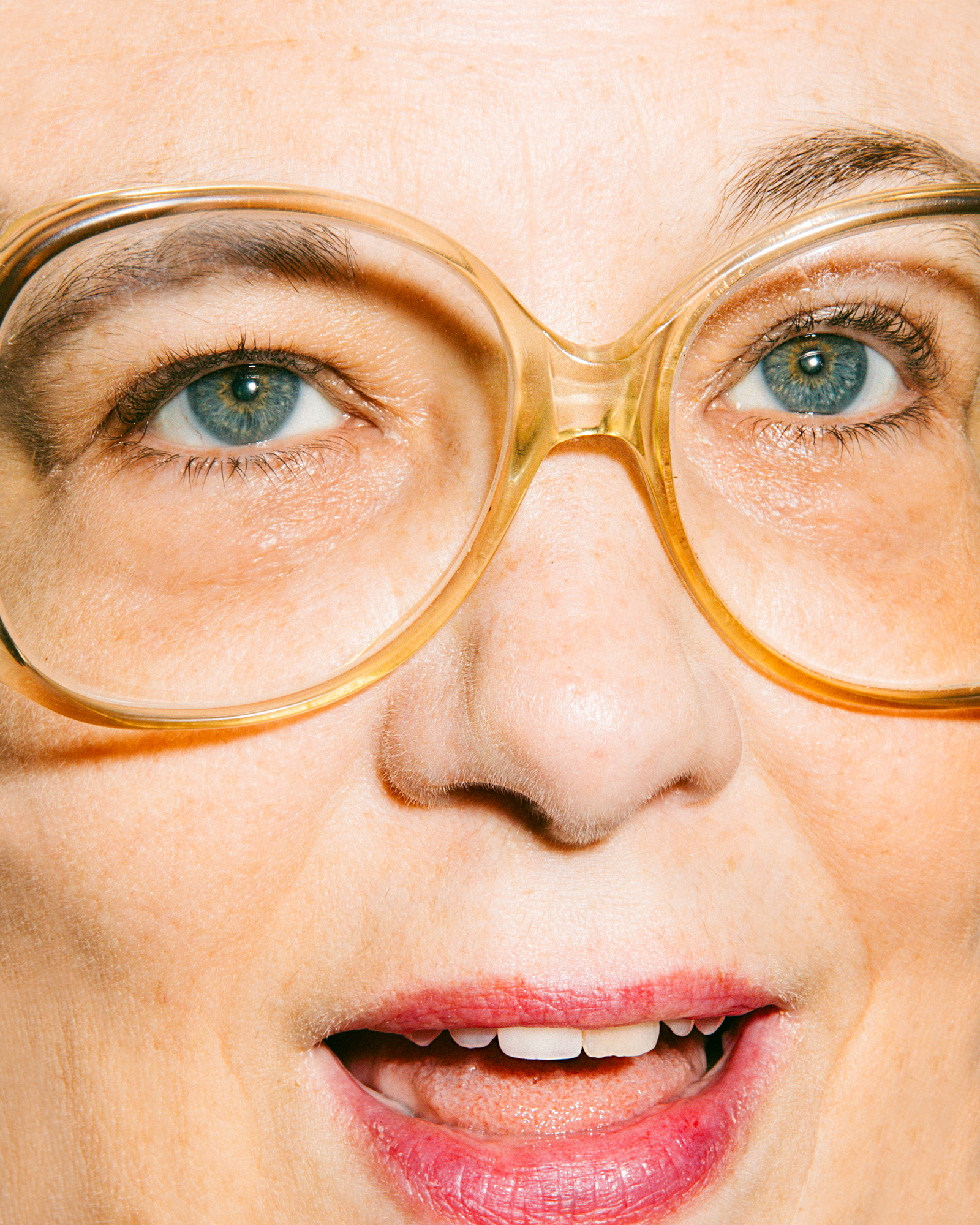 a super close up shot of an older woman's face, with bright pink lipstick and large acetate glasses