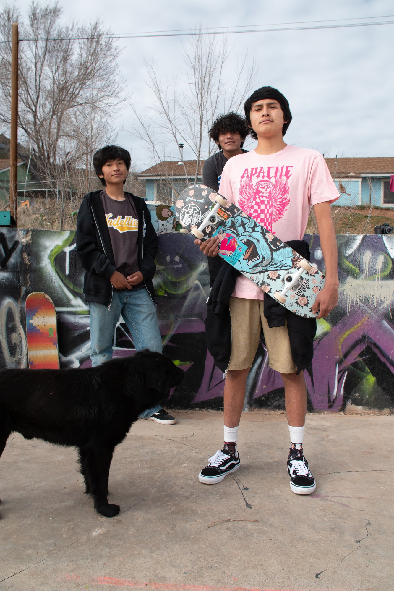 three young native skaters standing with their boards and a dog