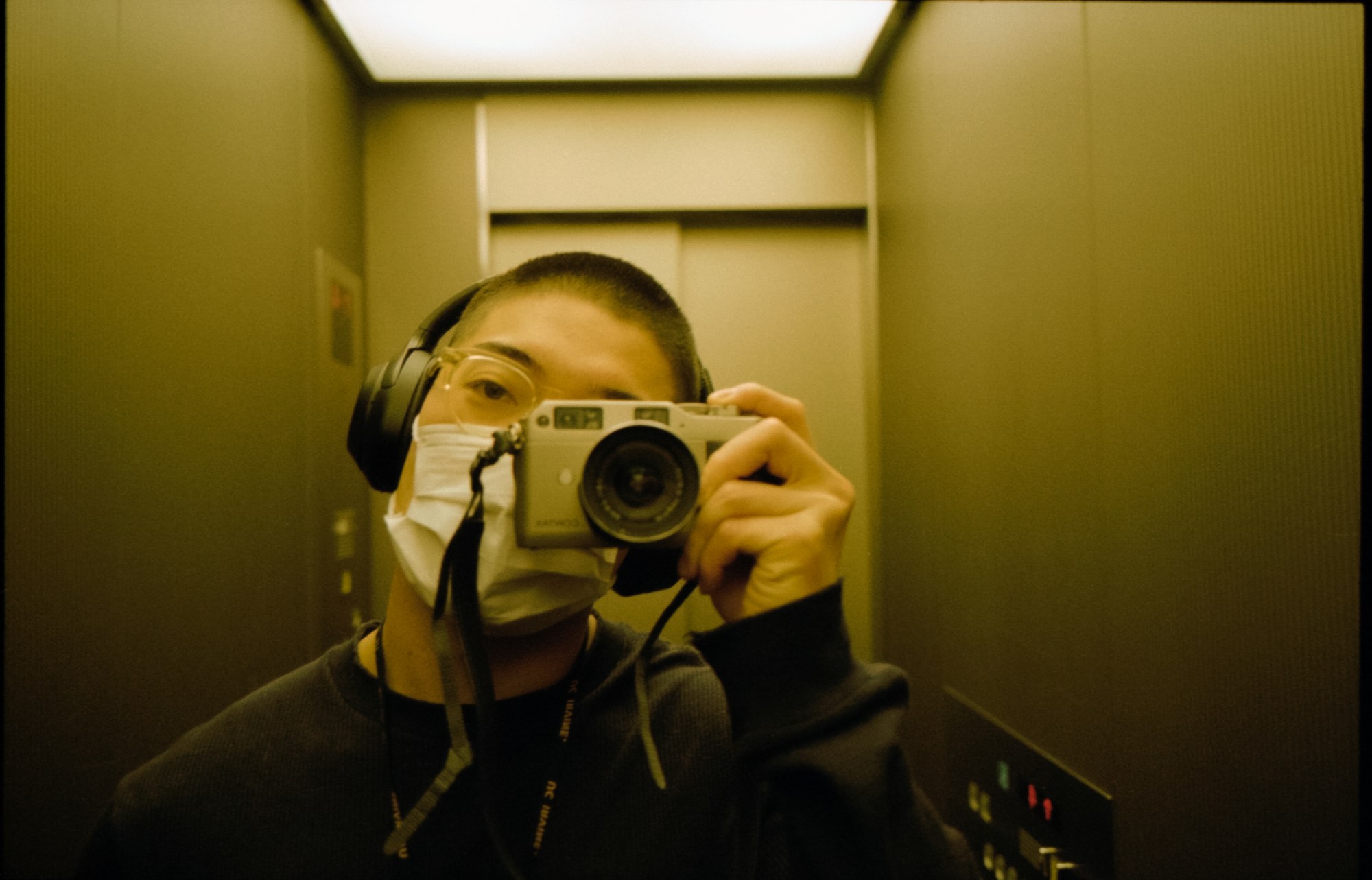 a man wearing a mask and headphones takes a mirror selfie in a list