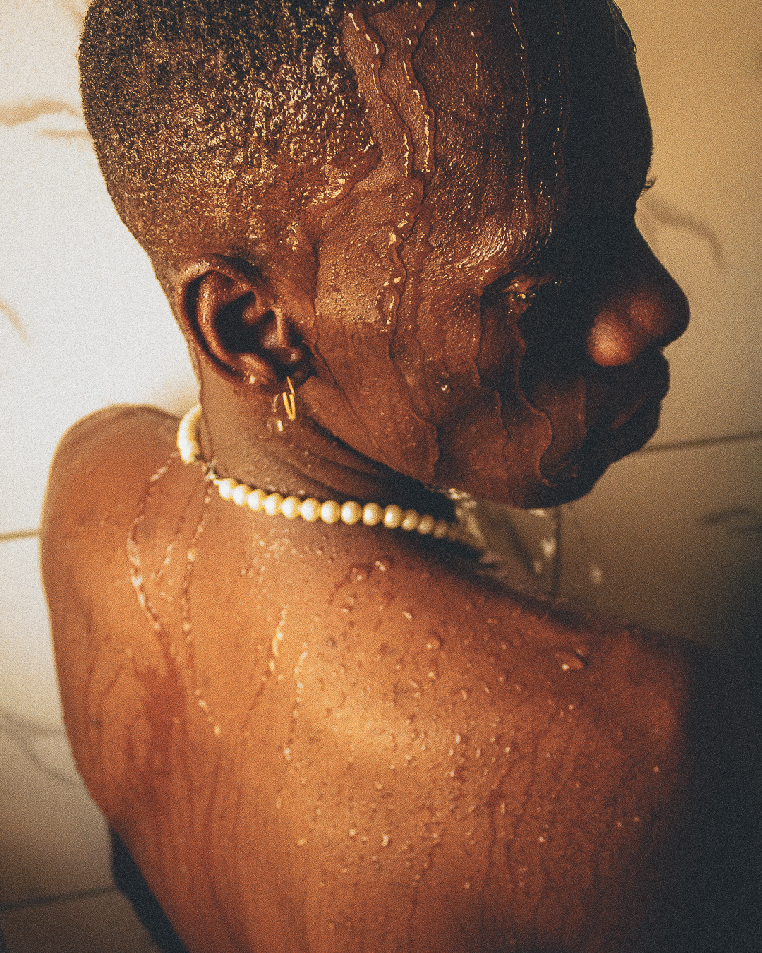 a person wearing a string of pearls in the shower. taken from behind, they look over their shoulder