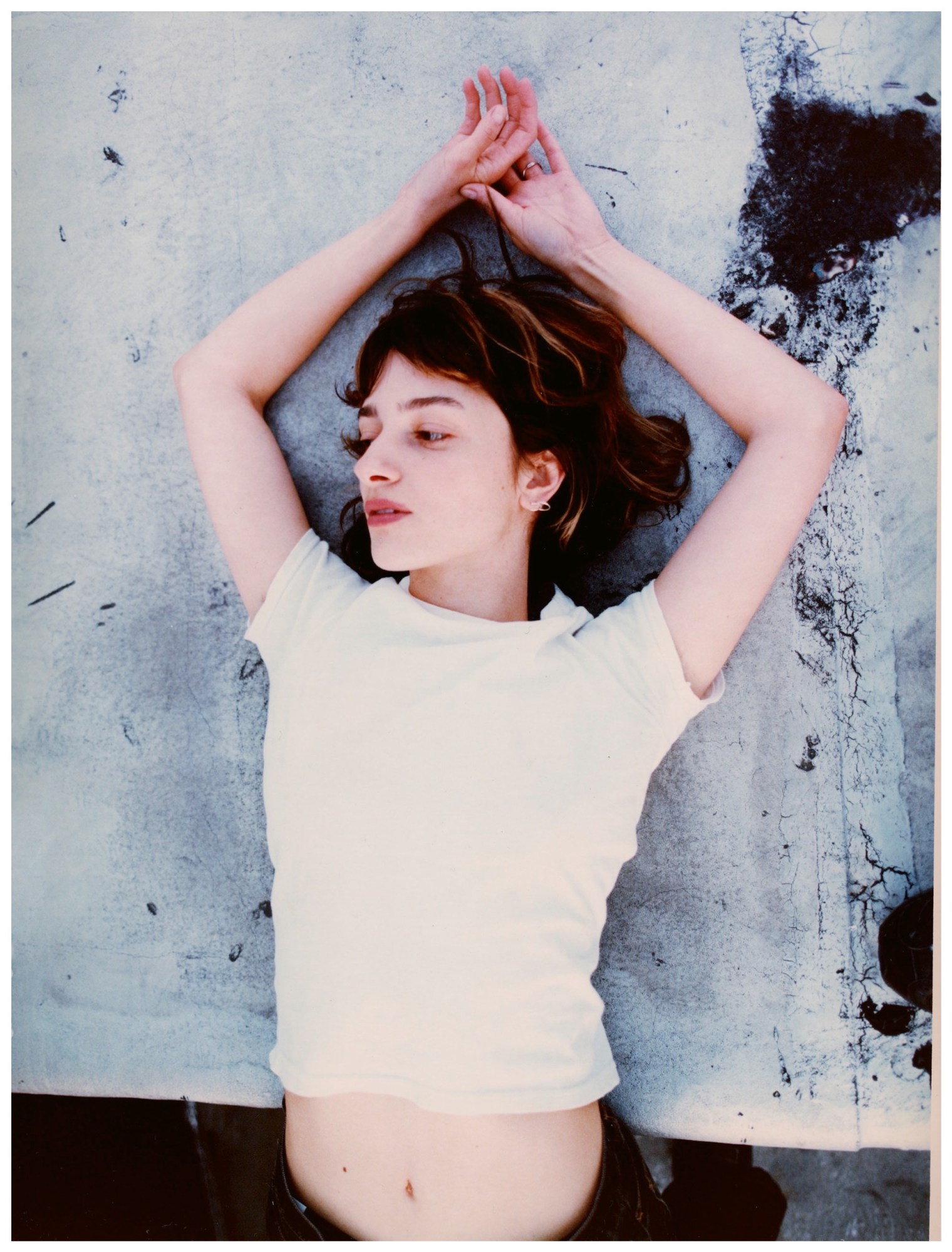 a woman leans backwards over a white painted surface, her hands behind her head and her stomach exposed