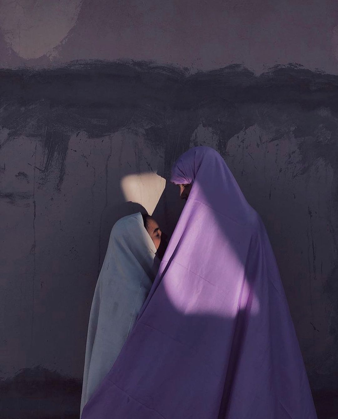 two women wearing white and purple chador coverings, a strip of sunlight lands on their faces