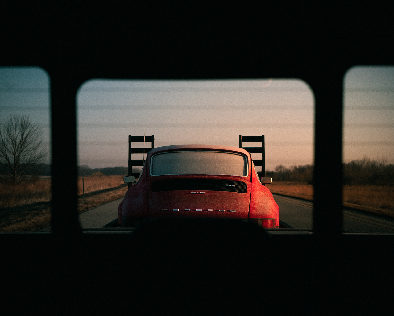 a red porche on the back of a truck, taken from the cab