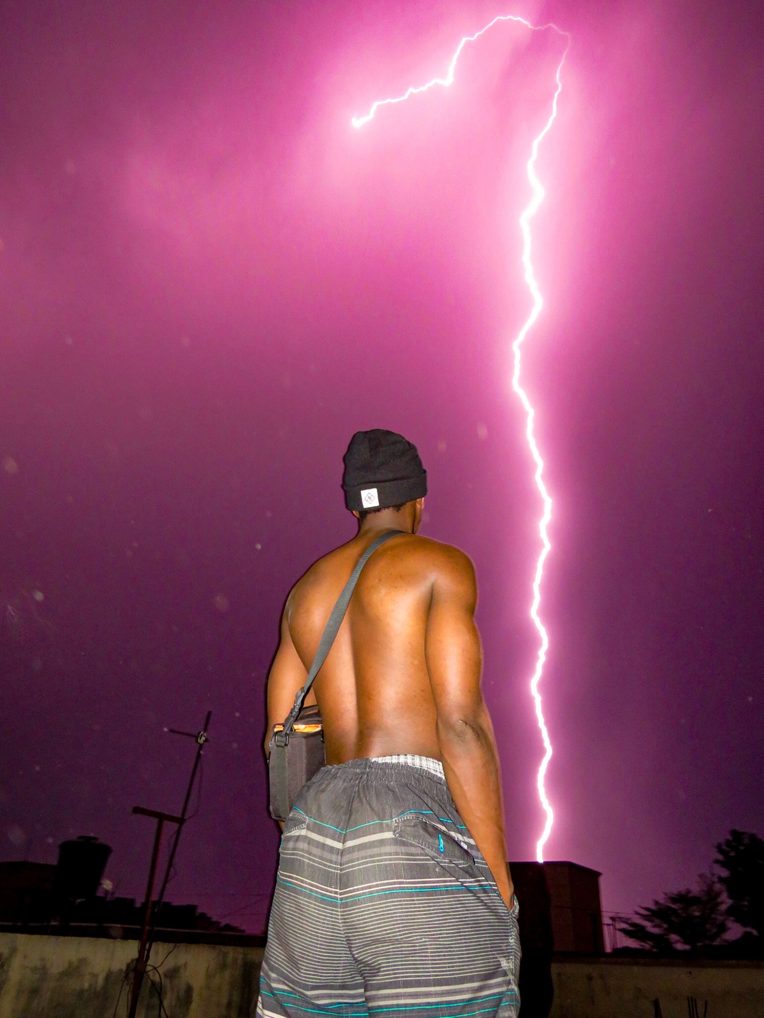 a topless man shot against a purple sky with a bolt of lightning almost reaching the ground