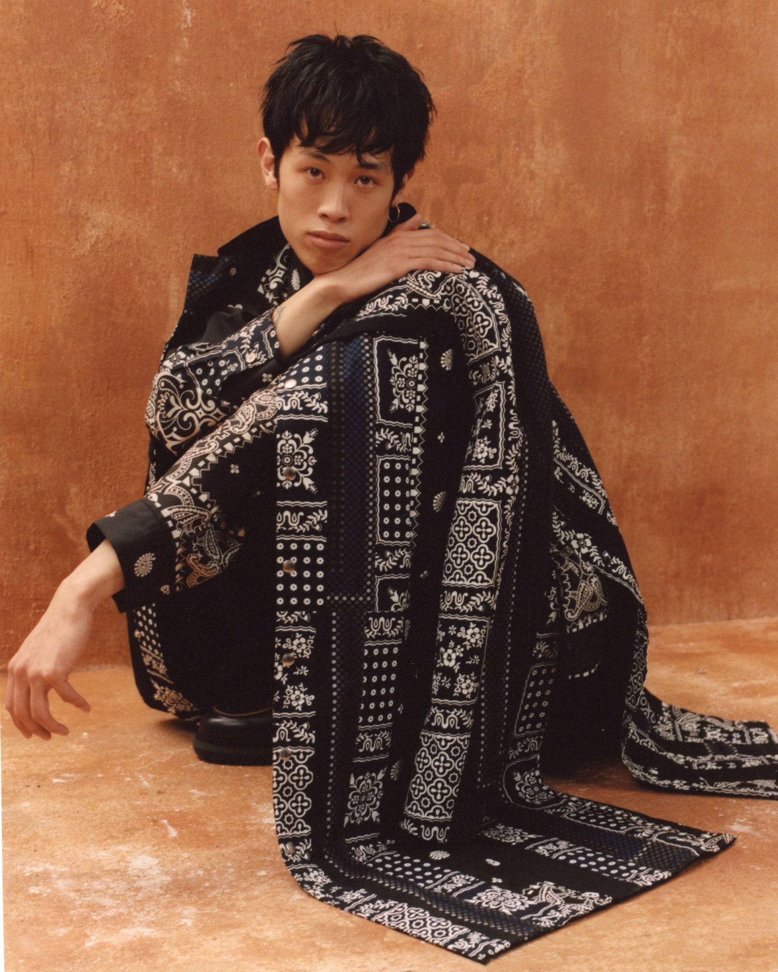 Leo Nguyen squatting in a long bandana printed robe