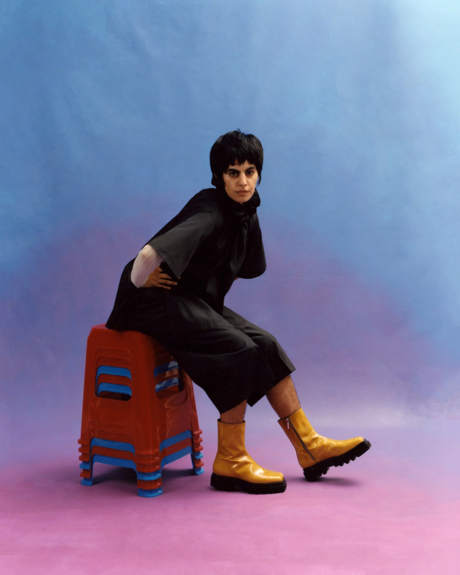 Jasdeep Kang sitting on red and blue stools with her hands on her hips