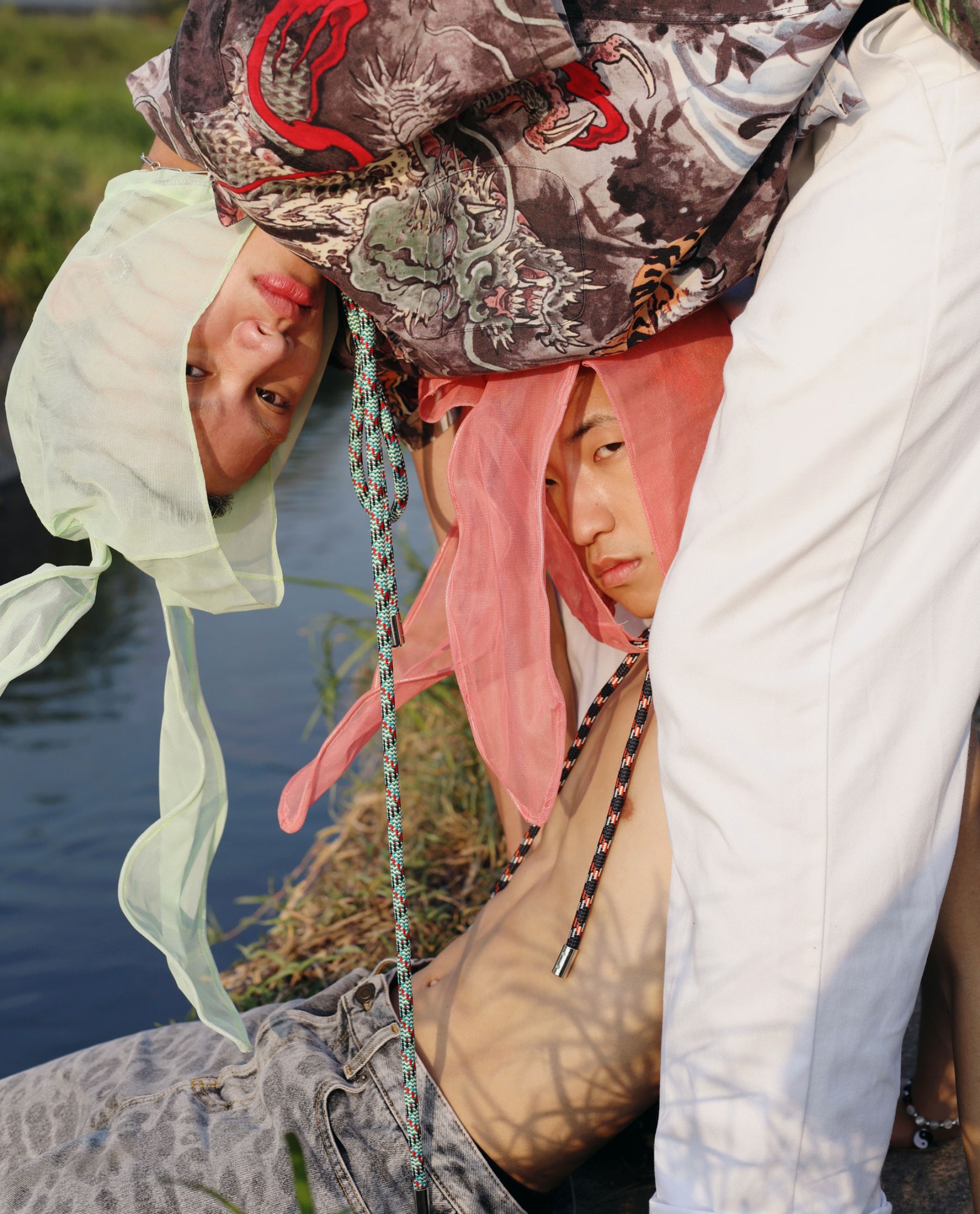 two young men wearing tulle bunny ears in pastel colours stand leaning over one another by a river