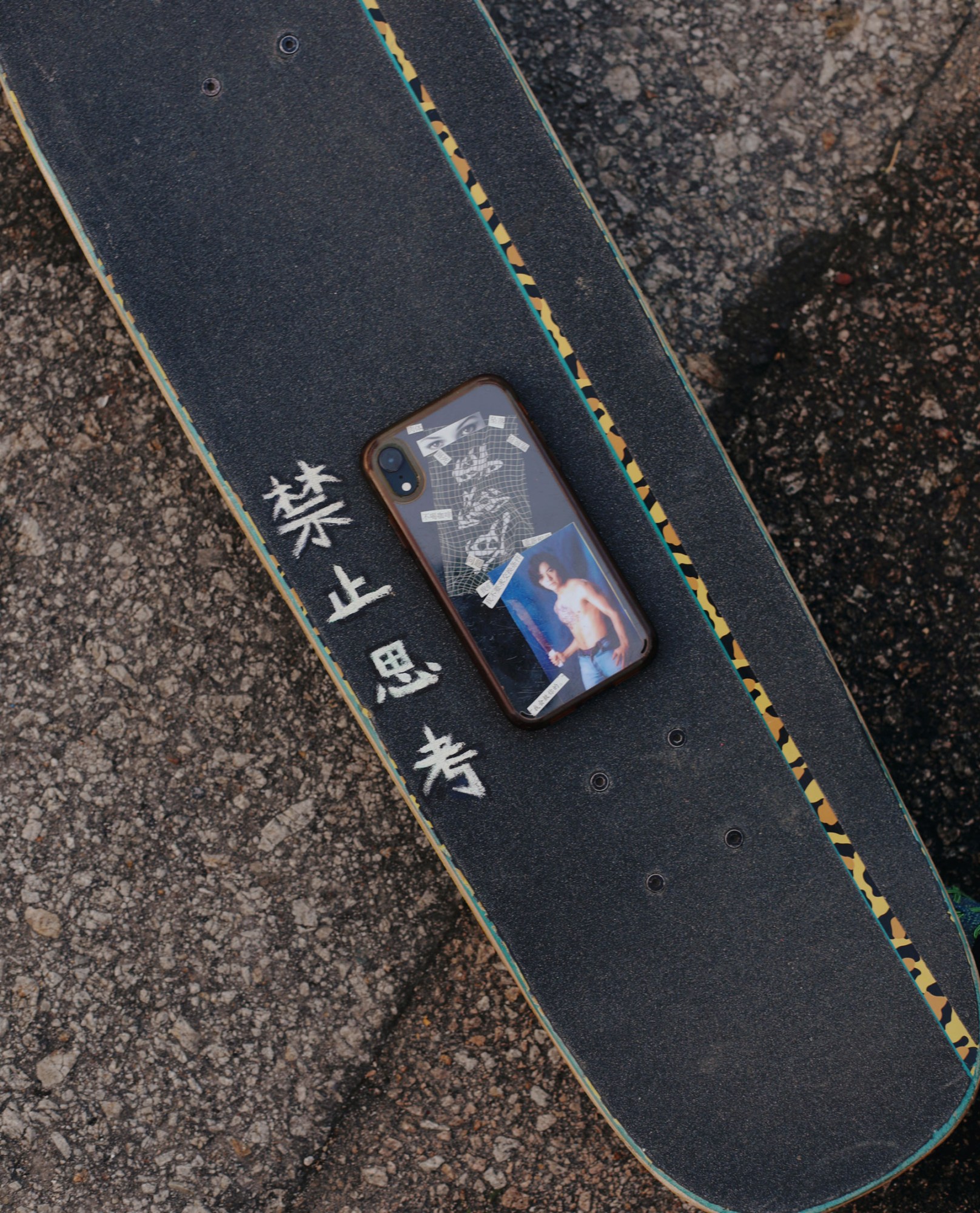 a phone with a DIY cut and paste cover featuring a man holding a machete lays on a skateboard deck