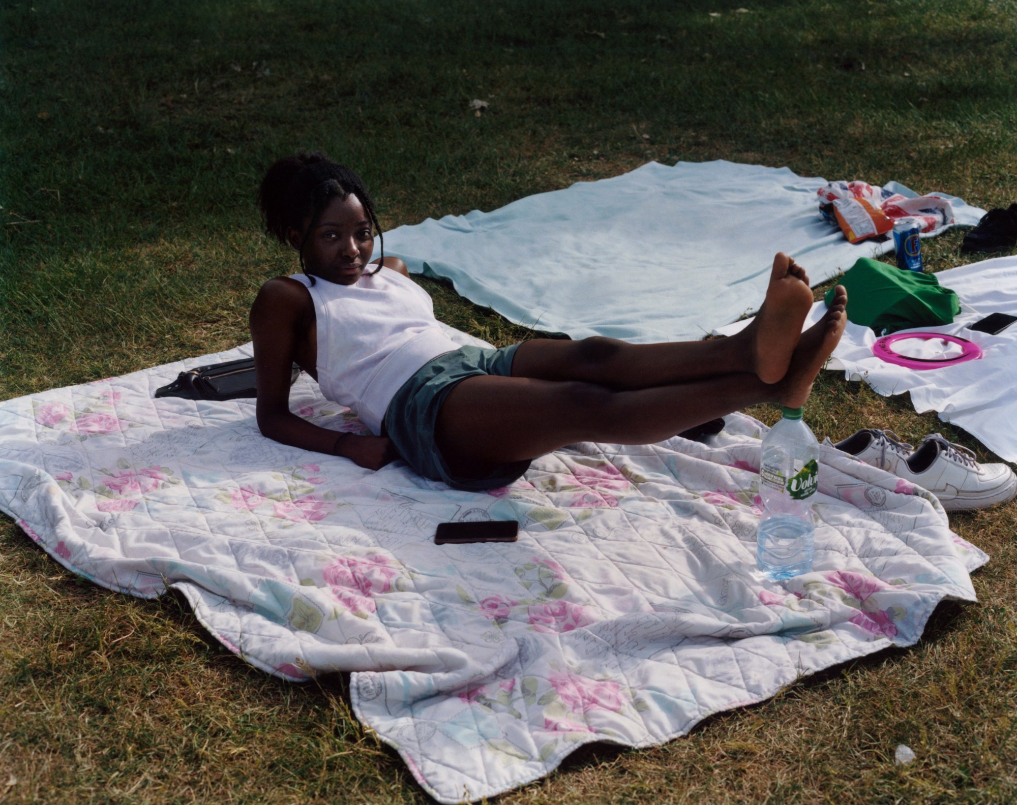 a girl lies on her back with her feet resting on a water bottle on a picnic blanket