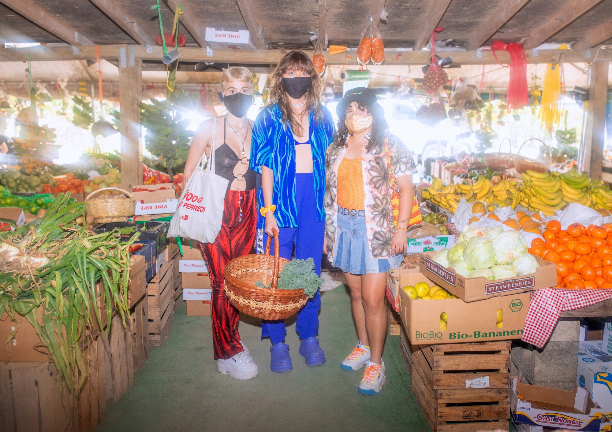 three girls standing in the outdoor fruit market holding a basket