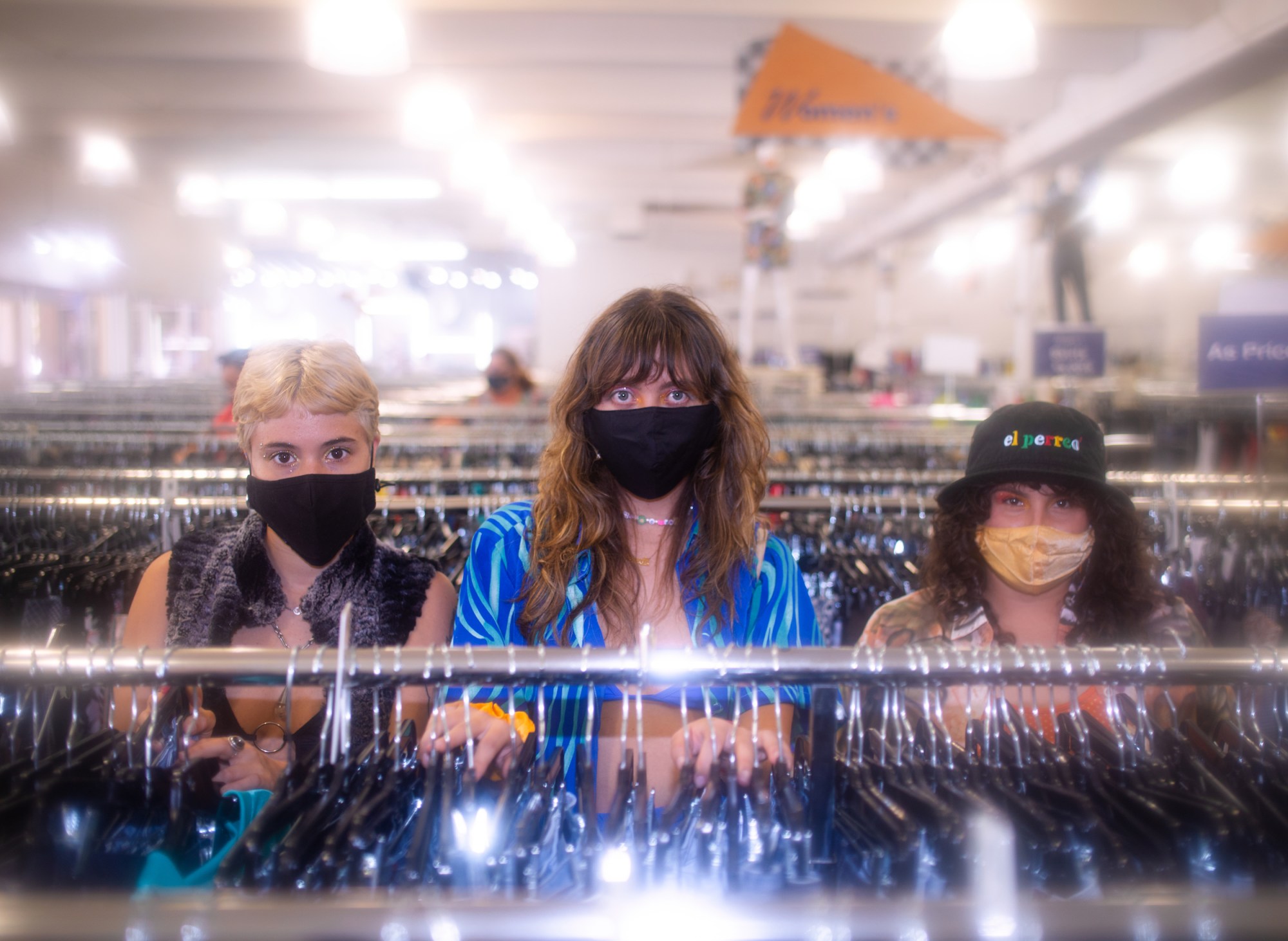 three girls standing in front of a clothing rack with masks on their faces