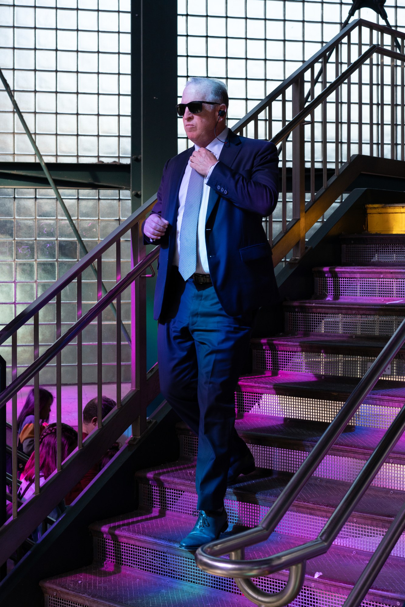 a man in a suit and dark sunglasses walks down the steps of a new york subway station