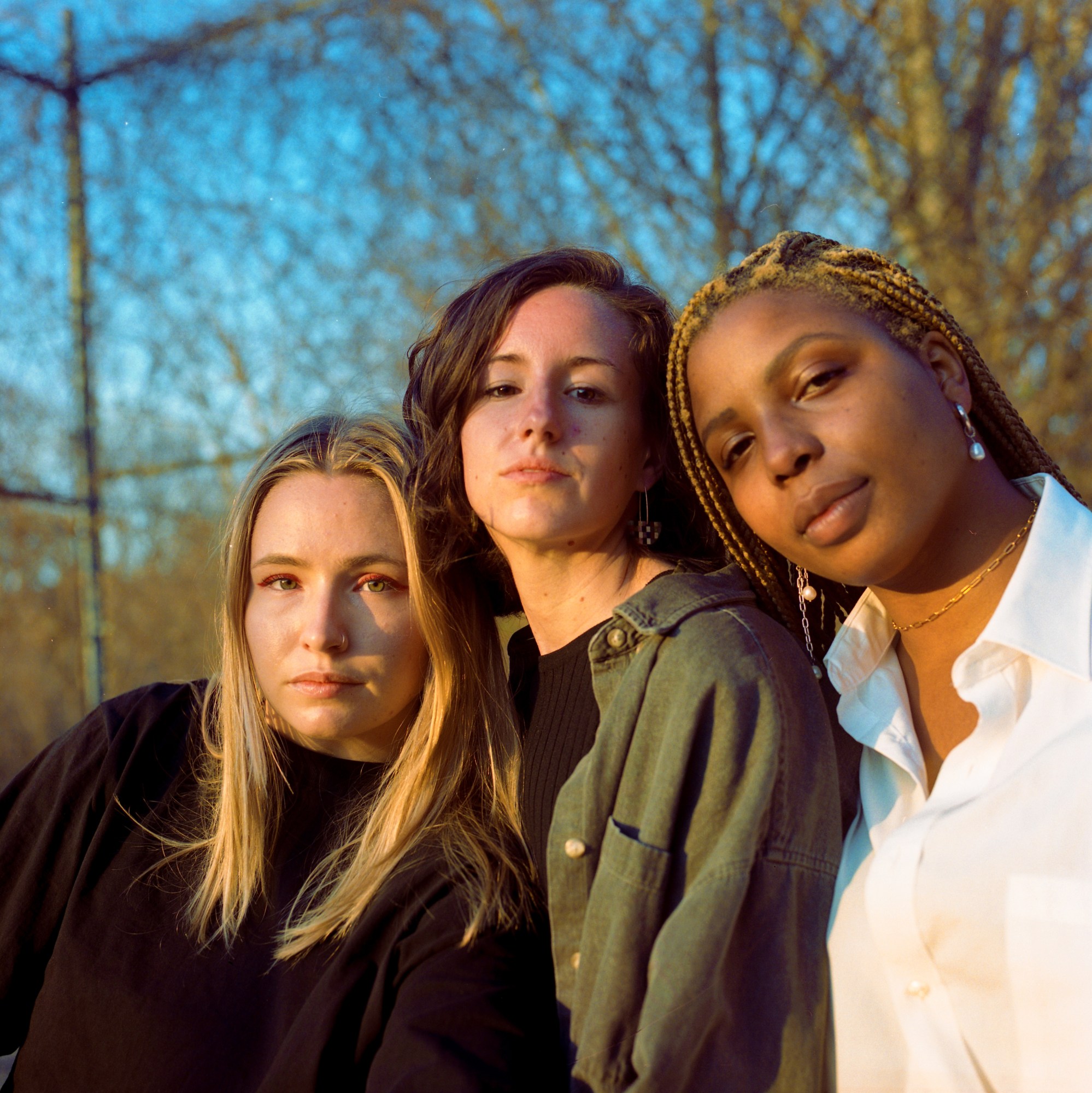 three women standing outside and leaning into each other looking at the camera