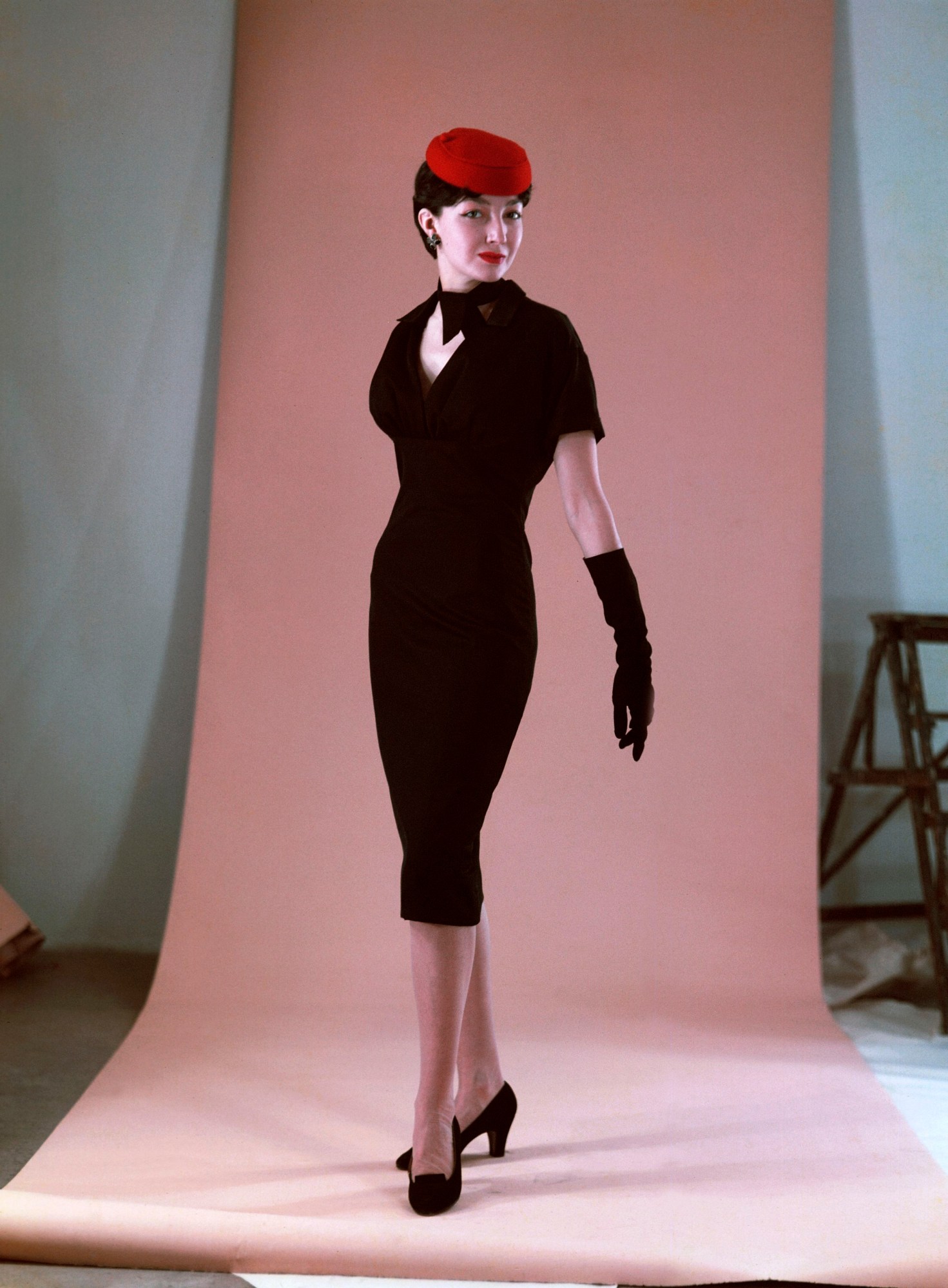 A woman wearing a fitted Black Dior Dress, shot against a light pink back drop