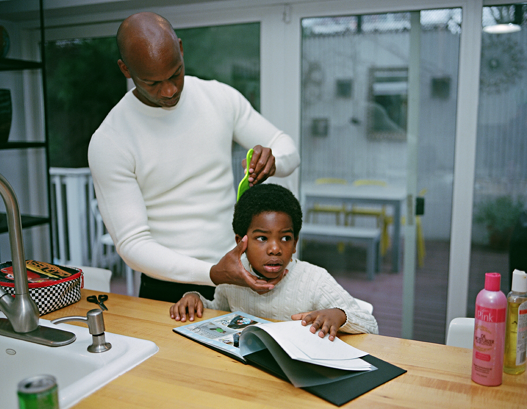 a father combs his son's hair as he reads a book