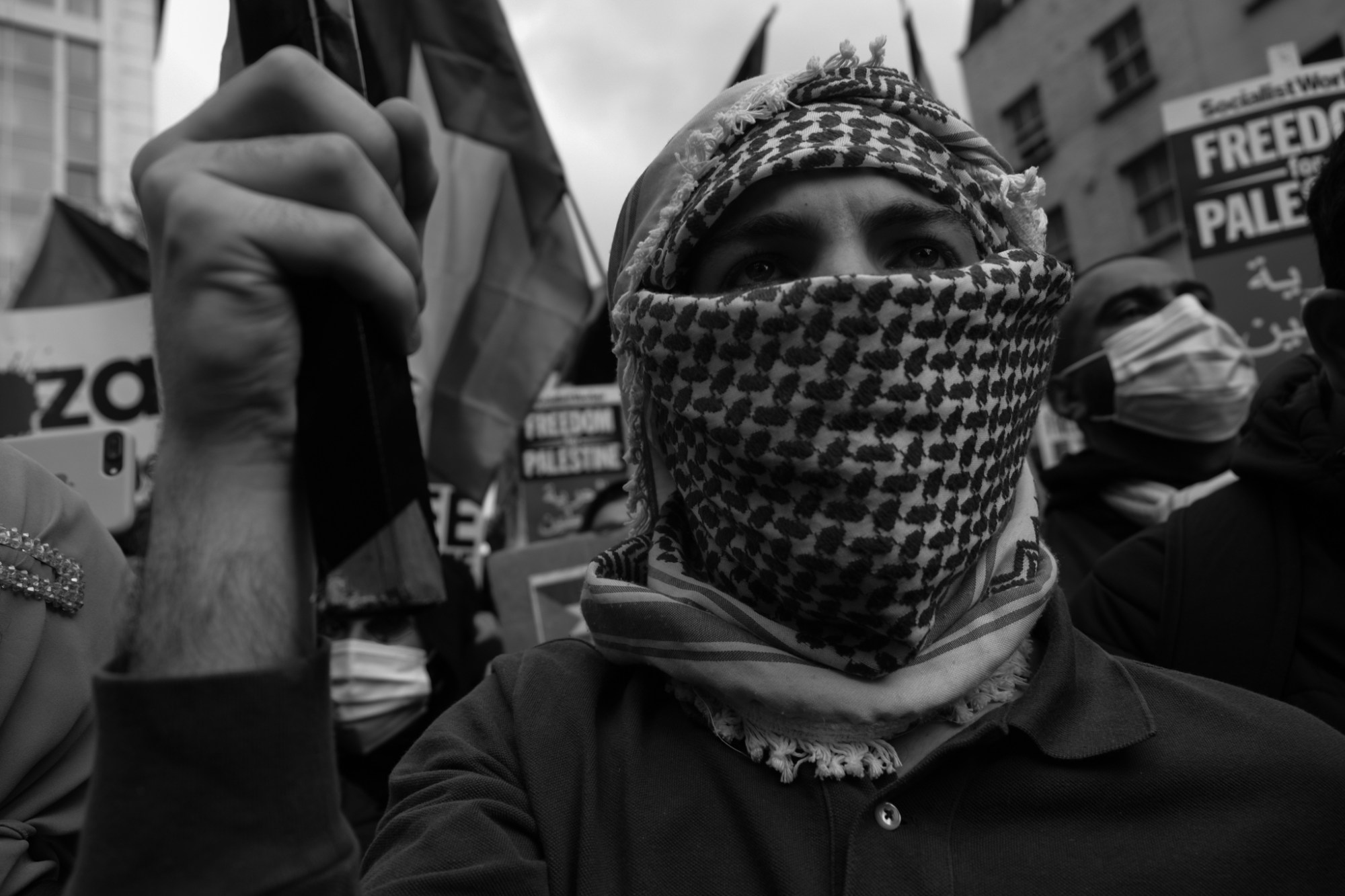 a masked person in a crowd holds a banner above the camera