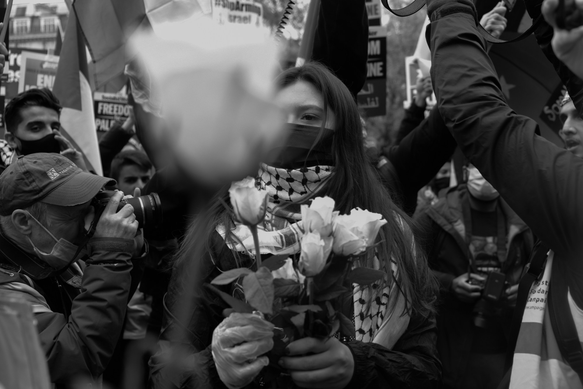 photographers shoot a masked woman handing out roses to peaceful protesters