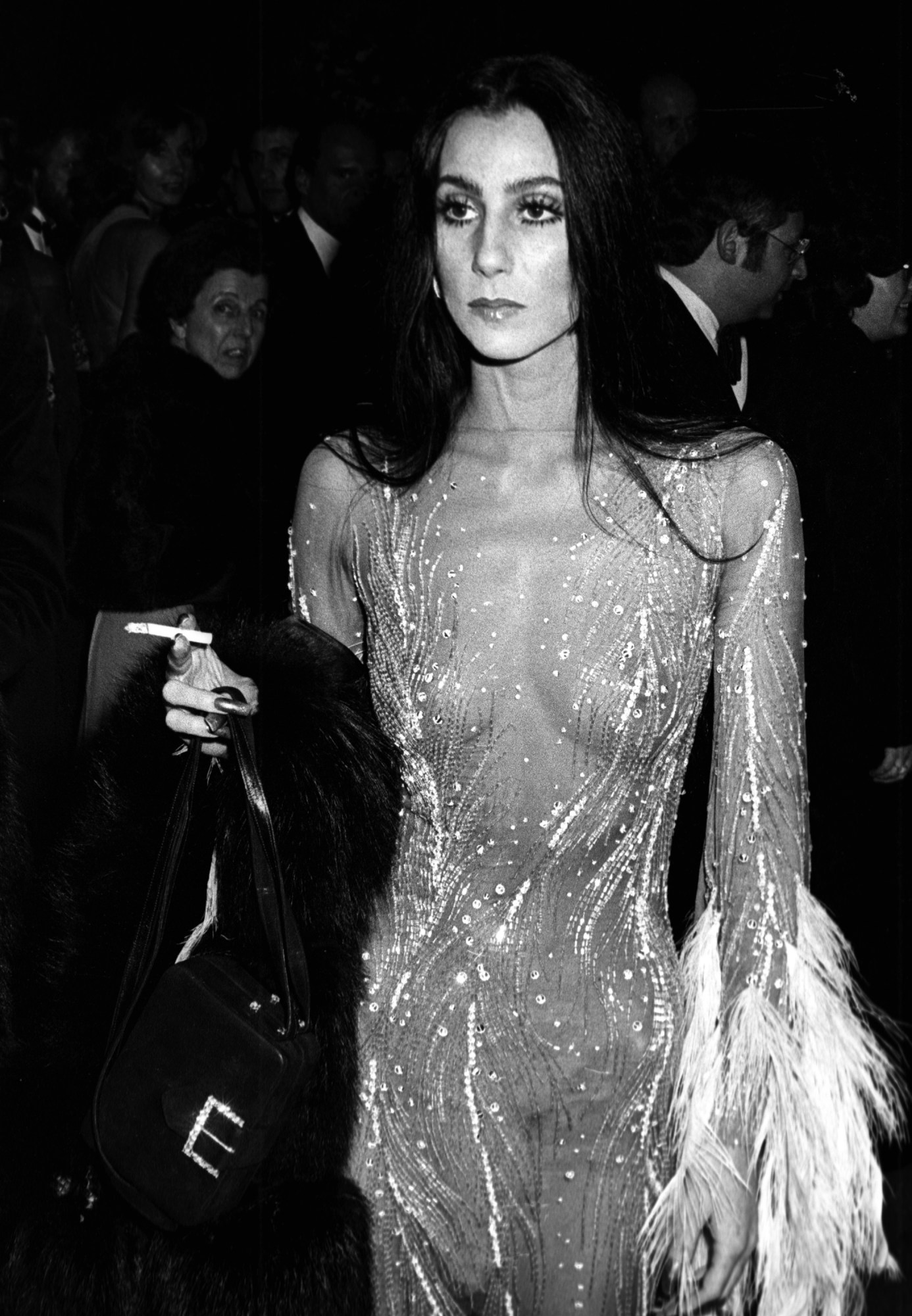 cher smoking a cigarette at the 1974 met gala in a sheer feather dress