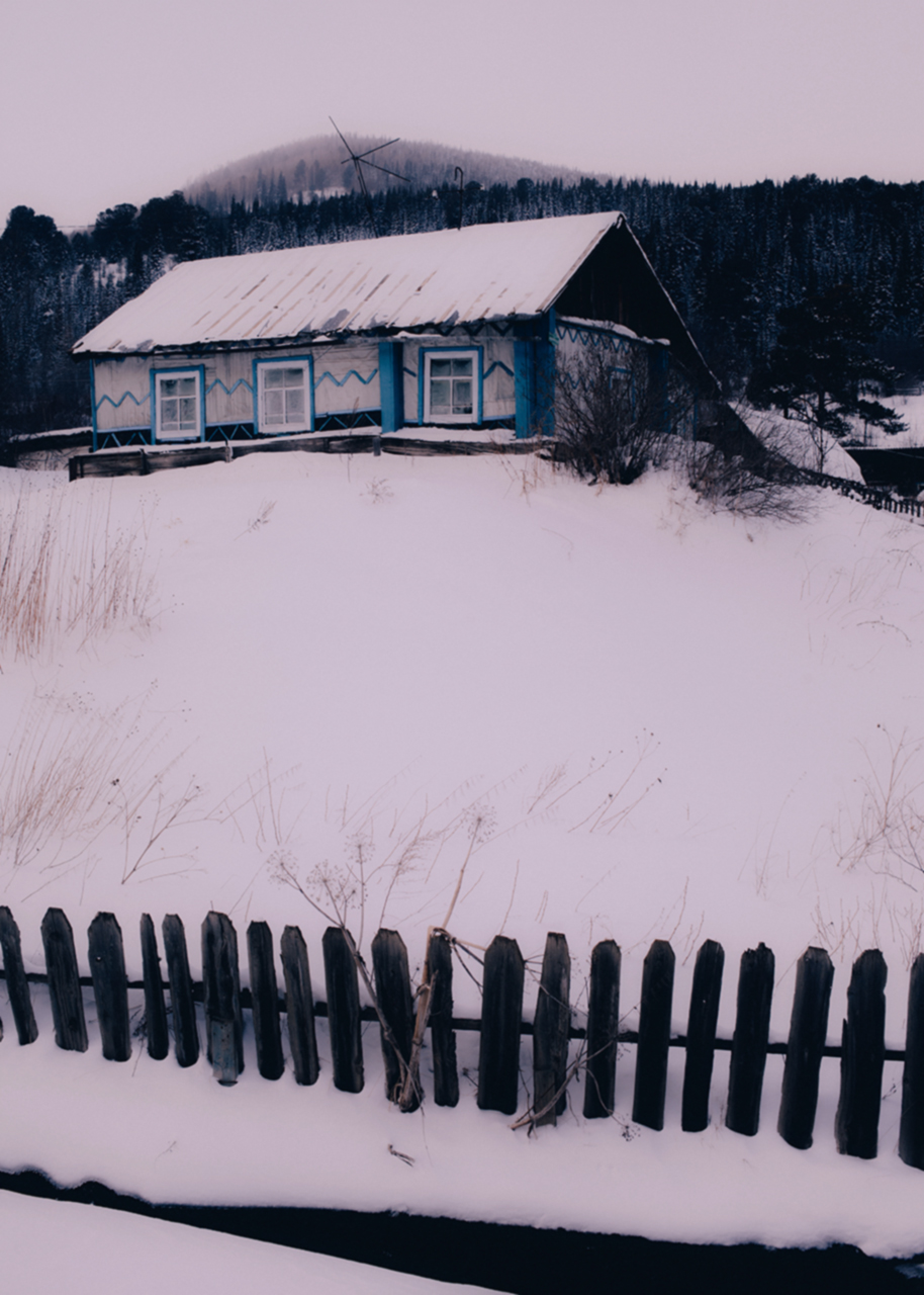 a siberian house raised up on a hill, surrounded by snow and trees