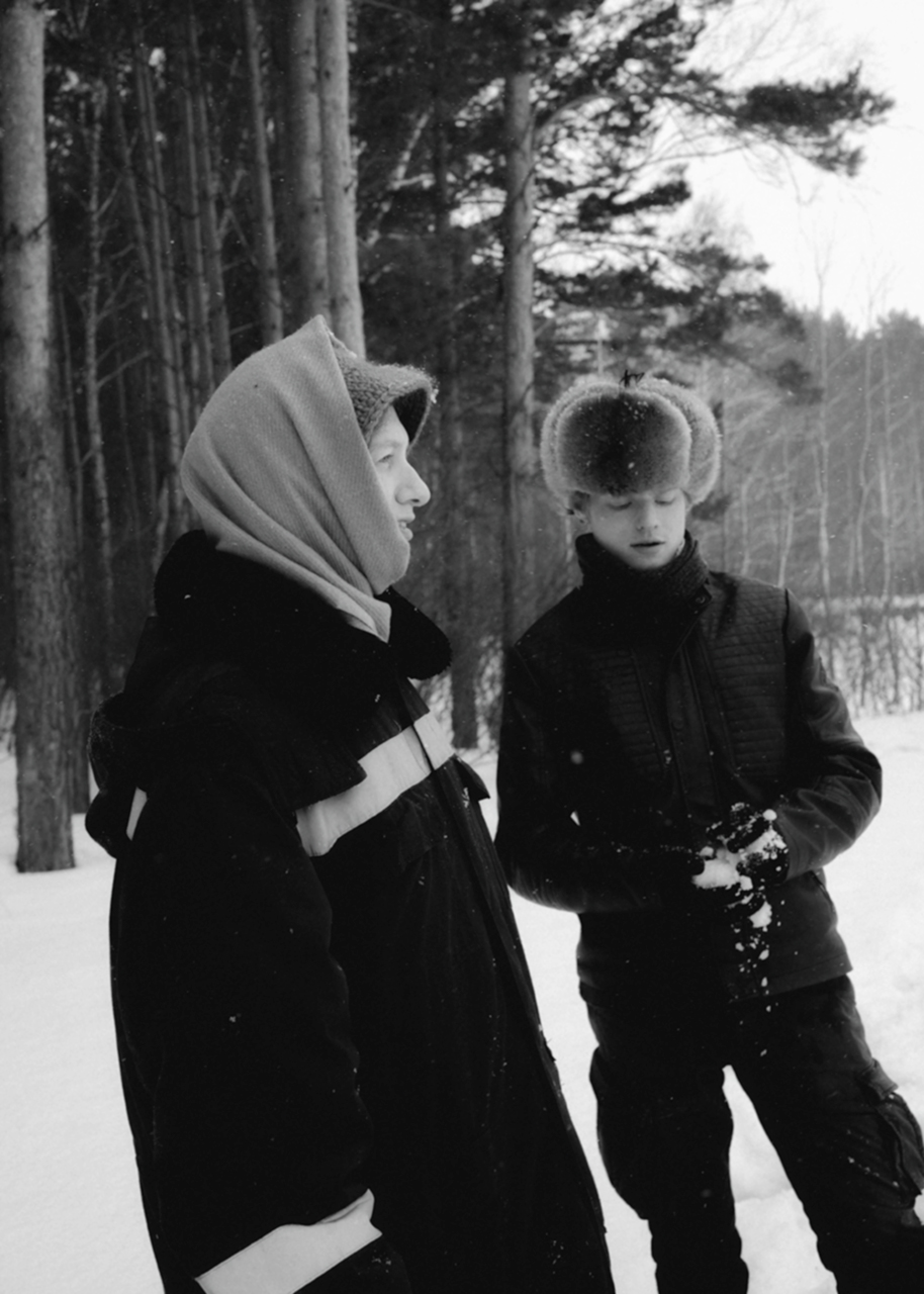 two young siberian men stand outside in the snow in heavy winter clothes