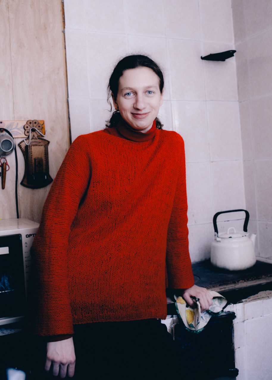 a young person in a bright red jumper stands in a kitchen