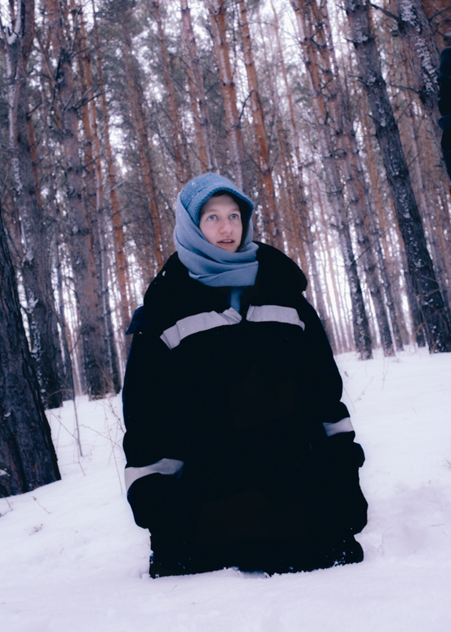 a young man stood in the woods with snow up to his thighs and a scarf around his head