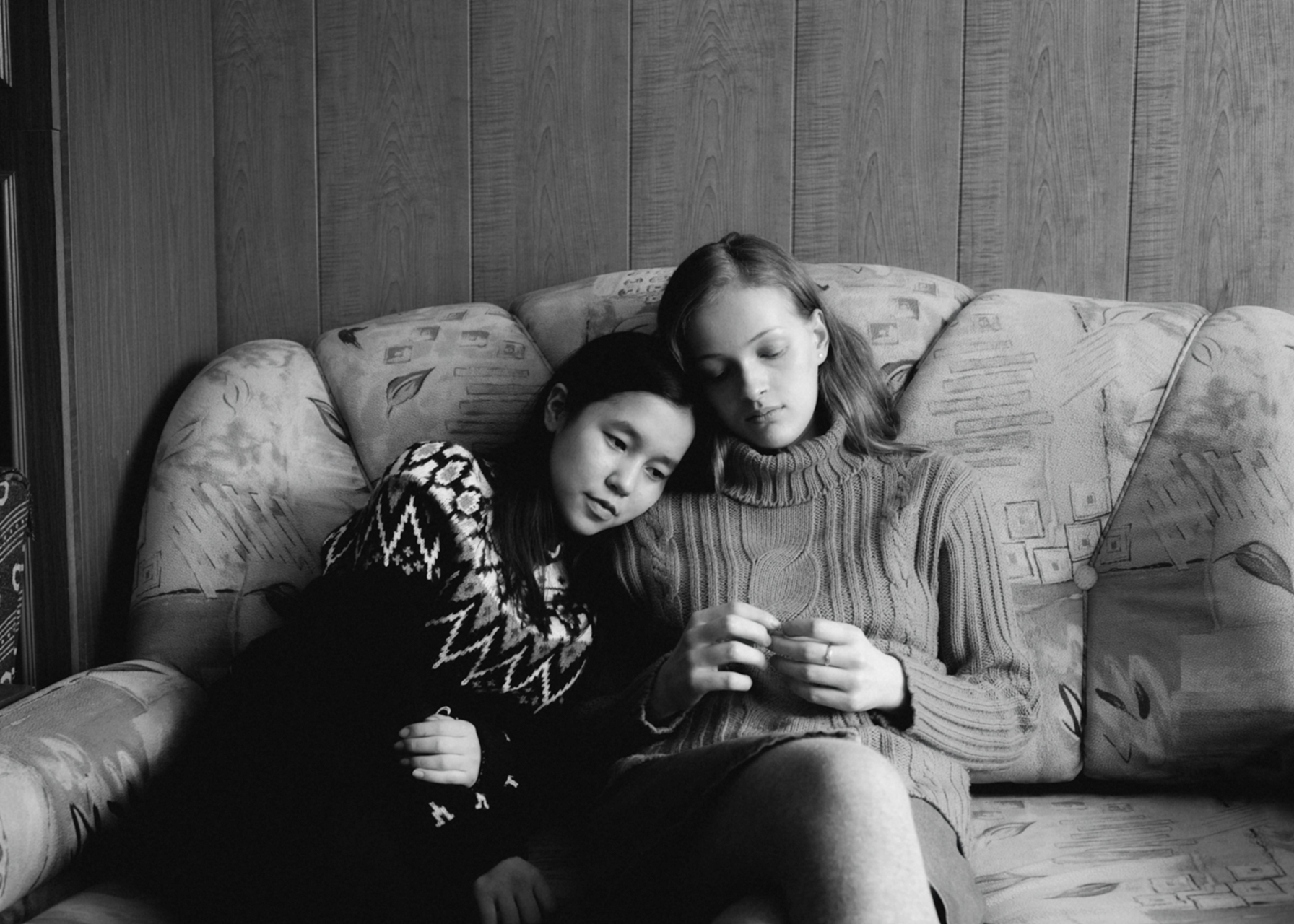 two young women rest upon each other on a sofa