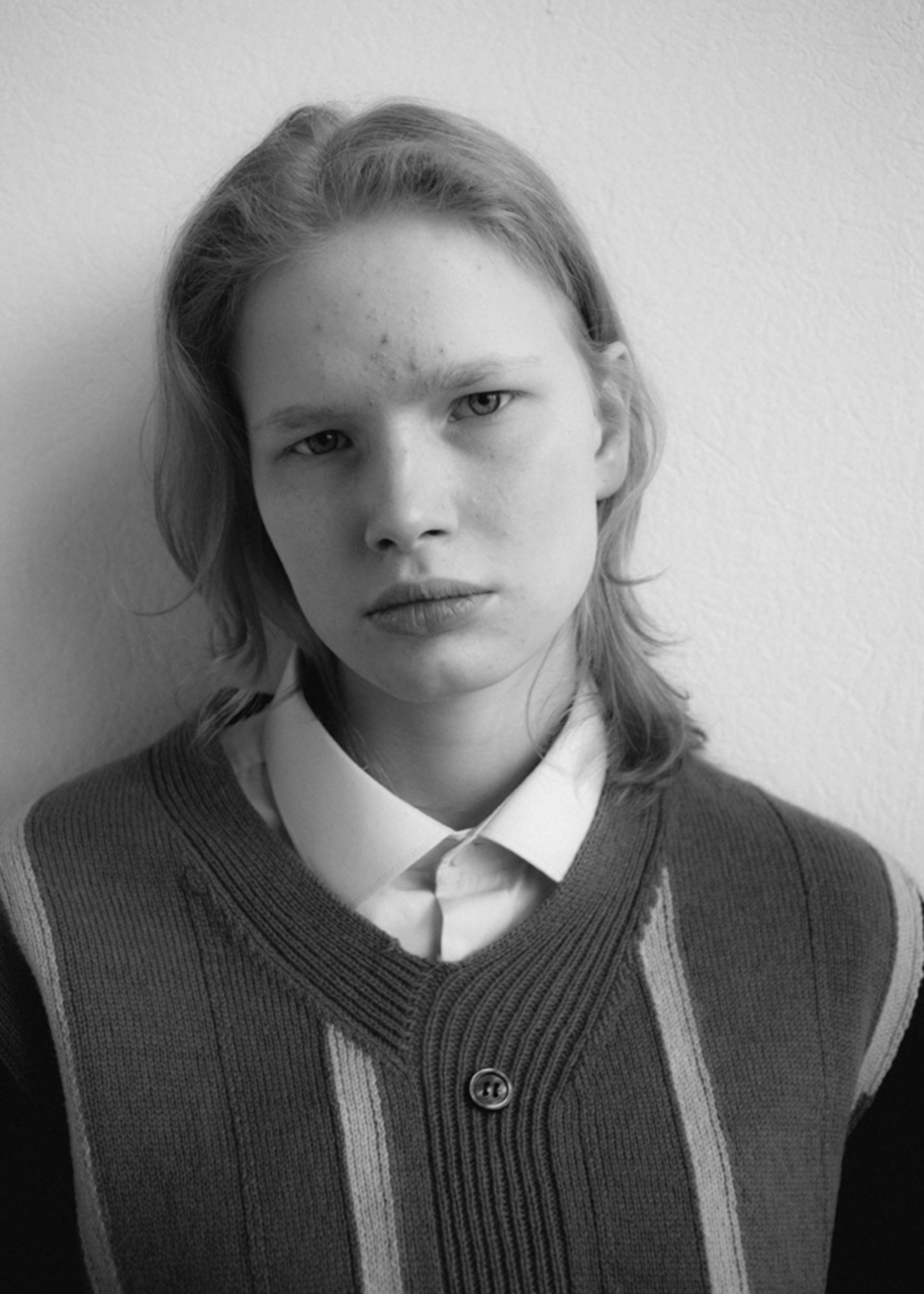 a young person stares deep into the camera, resting against a plain white wall