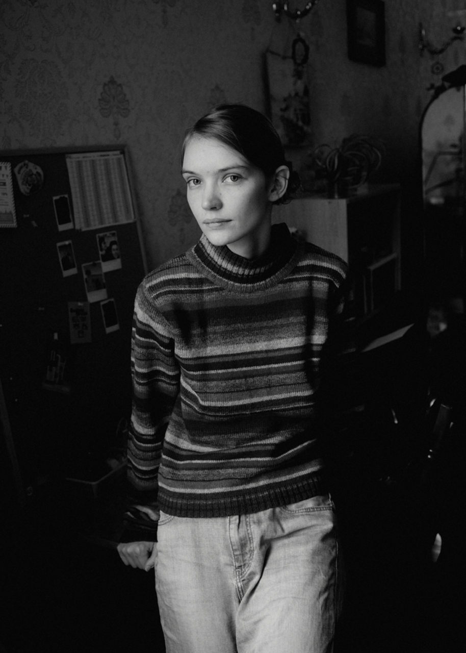 a young siberian woman rests against a table and looks into the camera