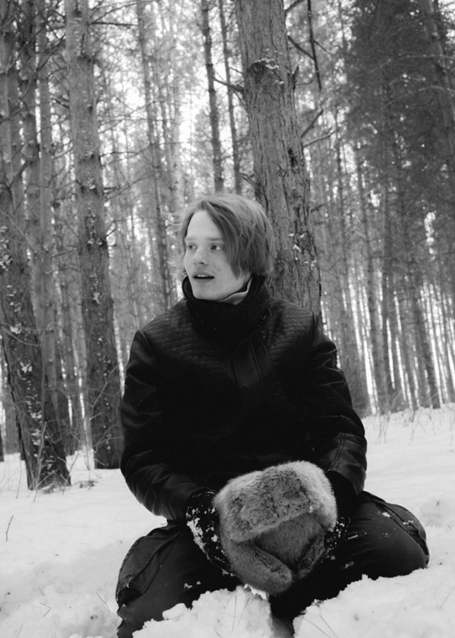 a young siberian man sits in the snow and holds a fur hat in his hands