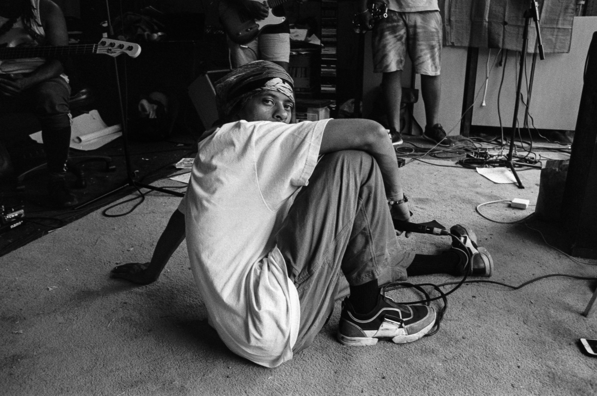 Pink Siifu sits on the floor holding a microphone, looking over his shoulder to camera