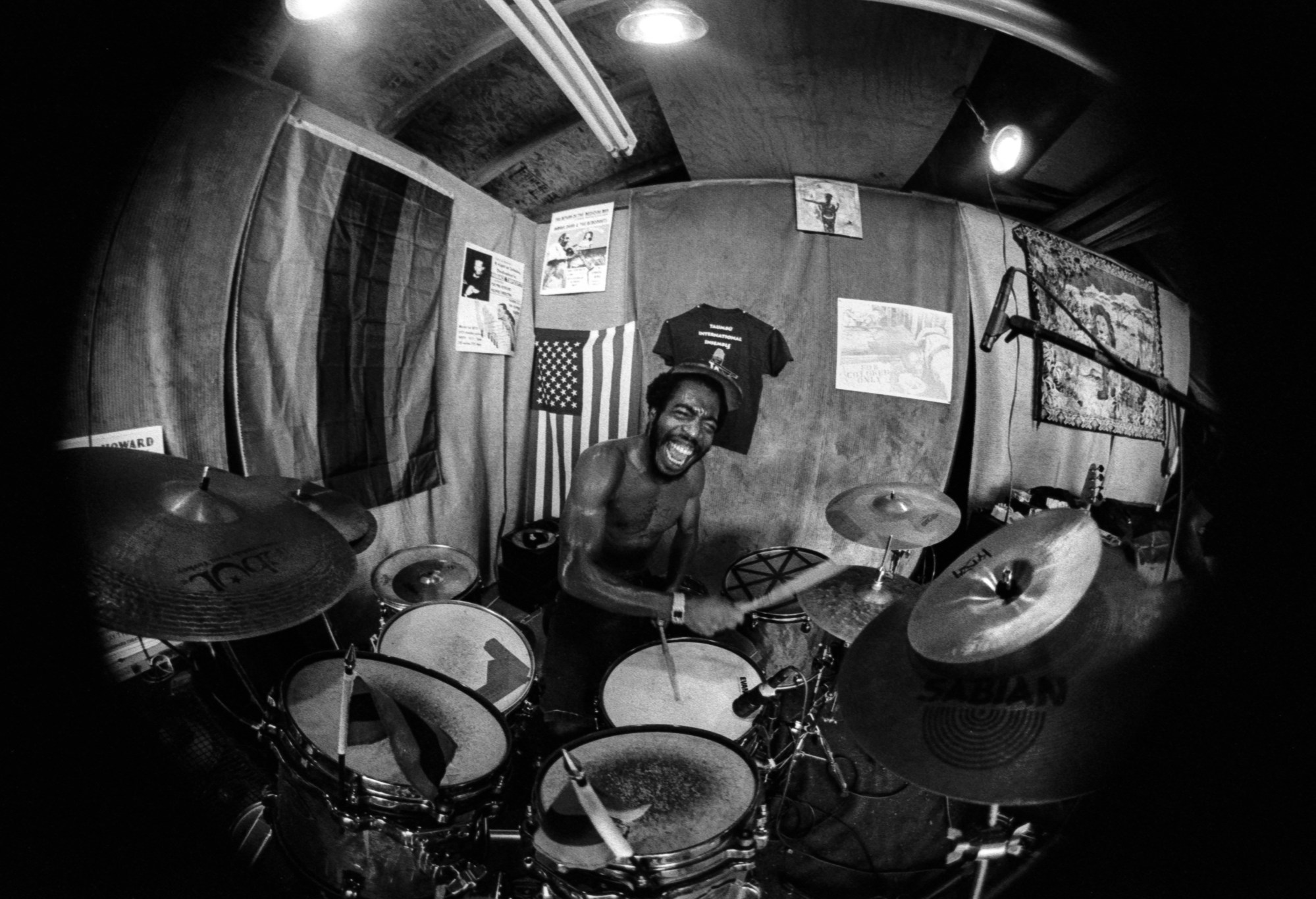 Mekala Session topless on the drums shot in black-and-white on a fisheye camera