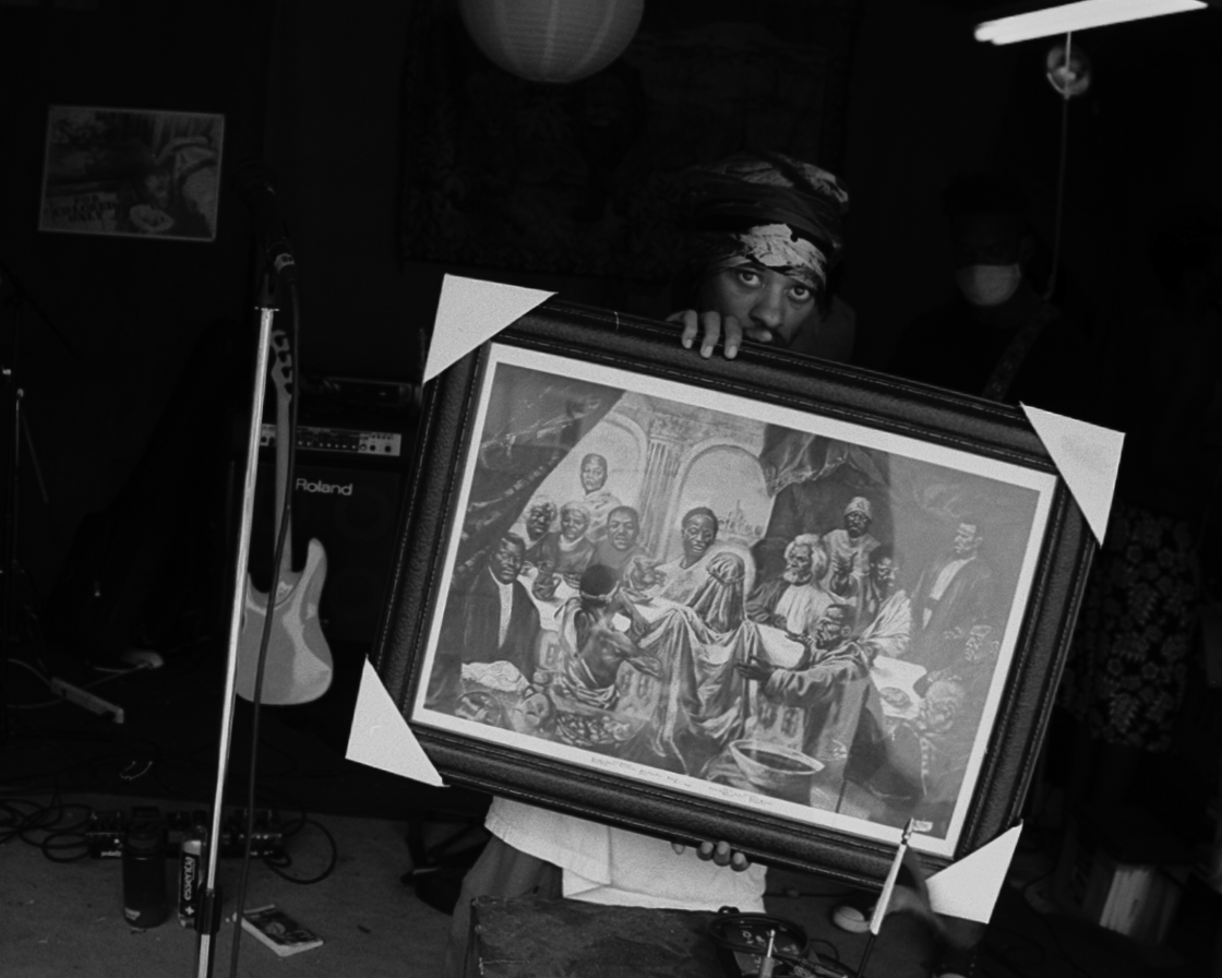 Pink Siifu holding up a framed painting of a religious scene